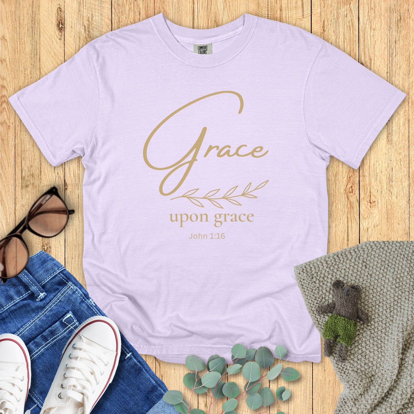 Orchid color t-shirt with 'Grace upon grace' text on a wooden surface with accessories.