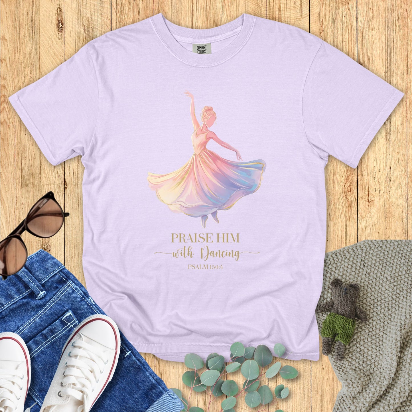 Lavender t-shirt with a colorful dancer graphic and text on a wooden surface with accessories.