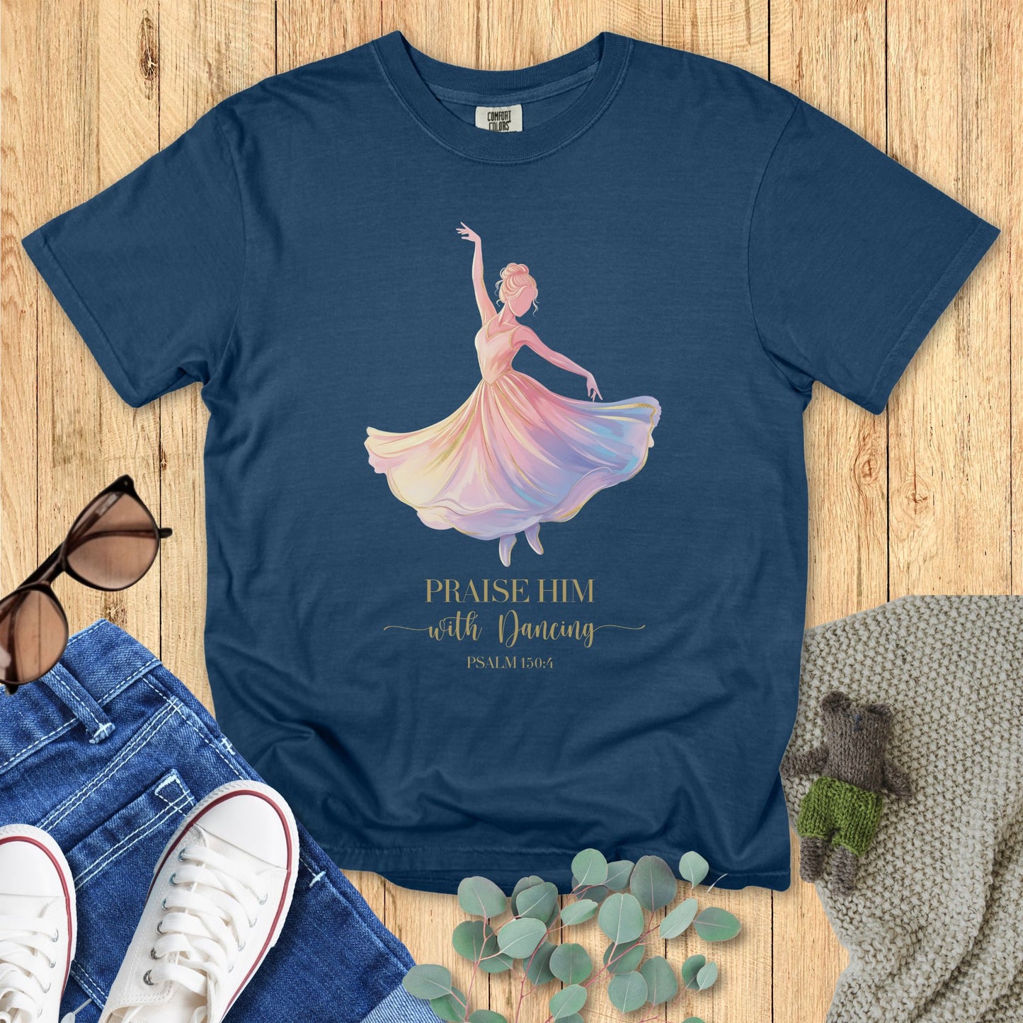 Blue t-shirt with a colorful dancer graphic and text on a wooden surface with accessories.