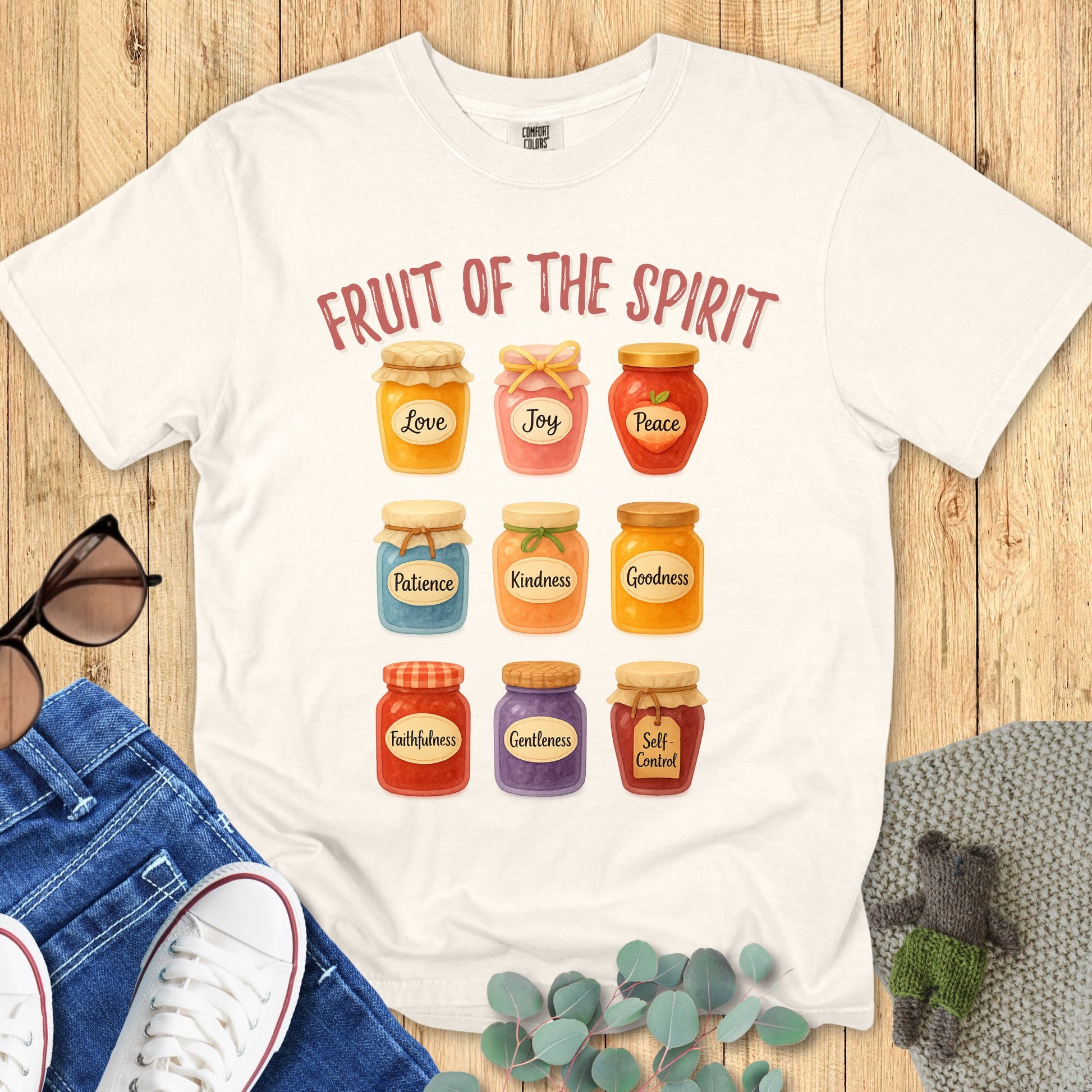 Comfort Colors 1717 Christian women t-shirt in ivory flat lay. Design features colorful jars labeled with the Fruit of the Spirit: Love, Joy, Peace, Patience, Kindness, Goodness, Faithfulness, Gentleness, and Self-Contro