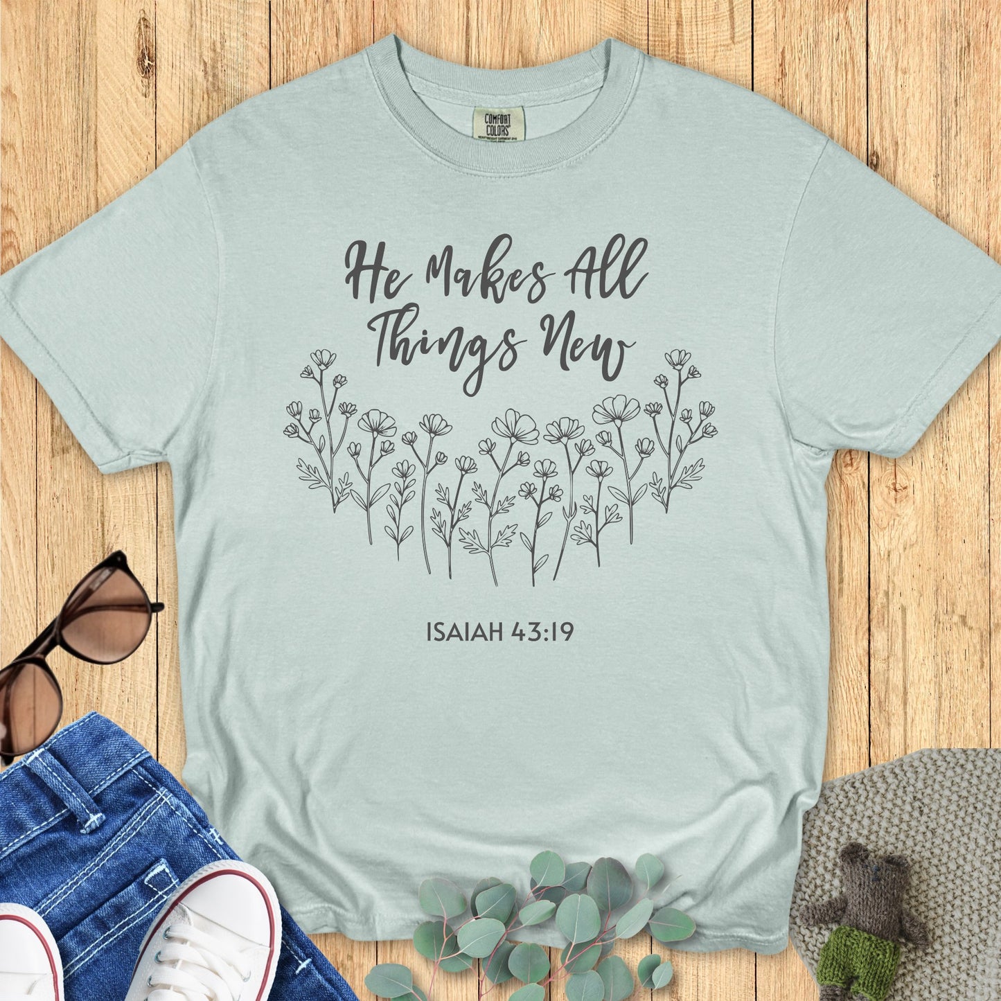 Comfort Colors 1717 Christian women t-shirt in bay green flat lay. Christian floral design with the words “He Makes All Things New – Isaiah 43:19” in script font