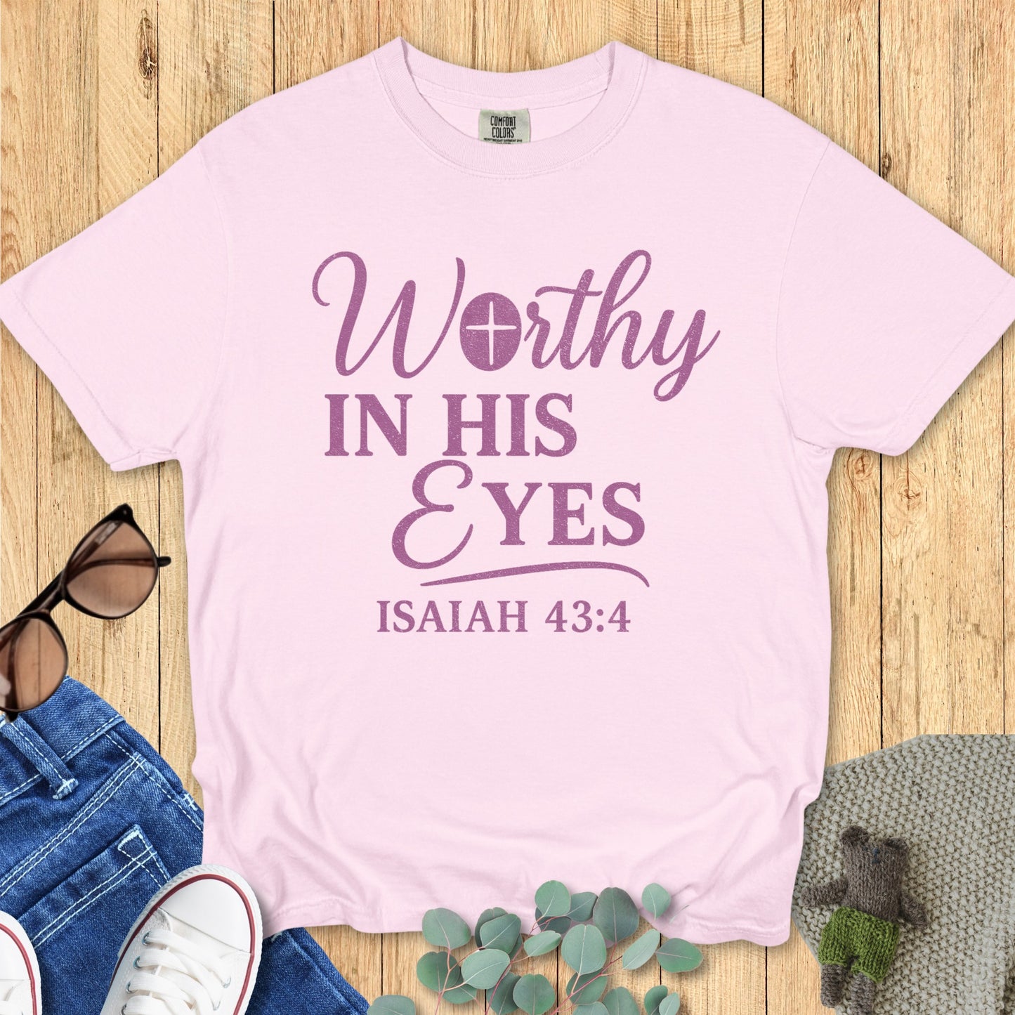 Comfort Colors 1717 blossom pink Christian t-shirt featuring the scripture 'Worthy in His Eyes – Isaiah 43:4' in purple text, presented in a flat lay with casual lifestyle accessories.