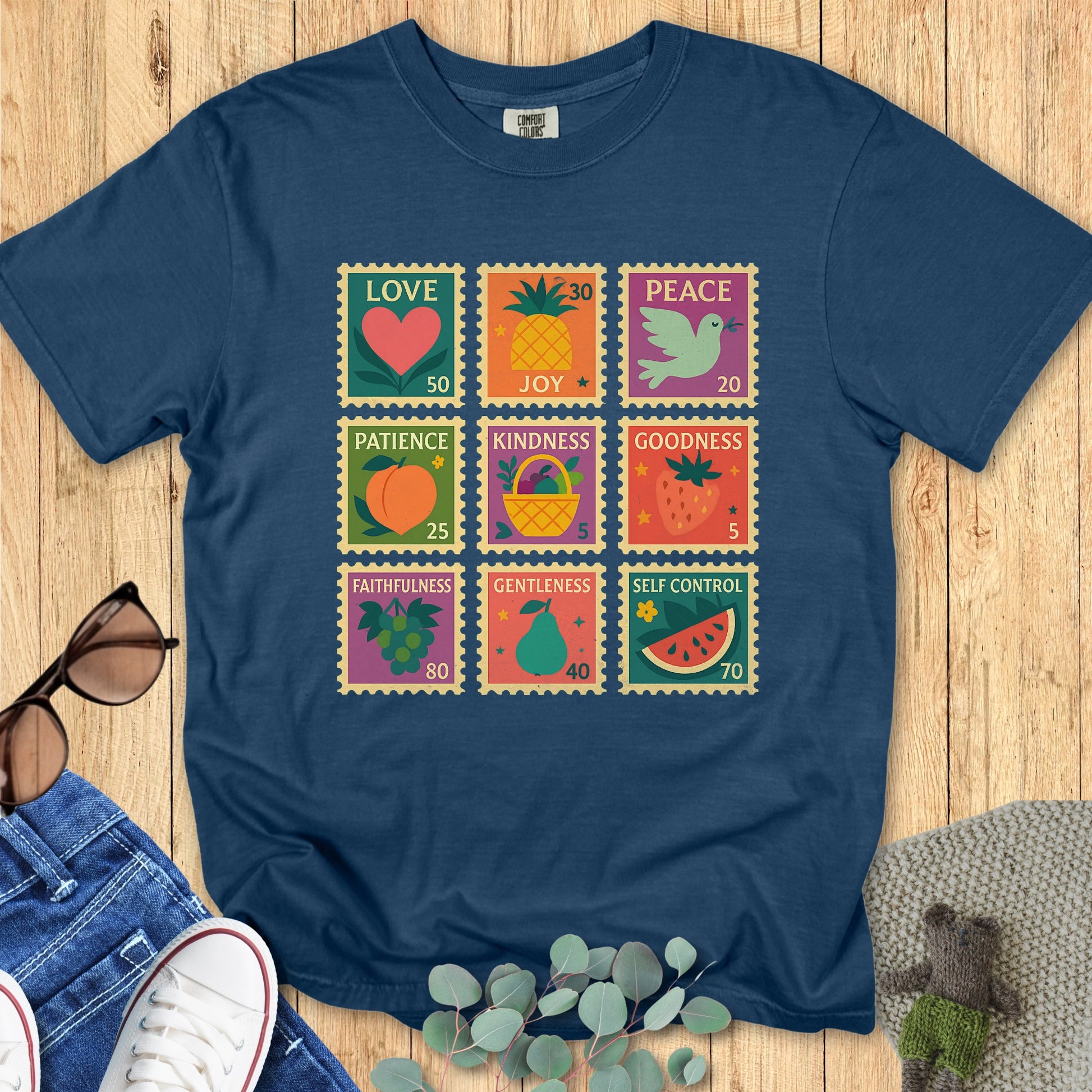 Flat lay of a Comfort Colors Christian T-shirt in midnight navy, showcasing a playful Fruit of the Spirit stamp design with vibrant fruit symbols and words: love, joy, peace, patience, kindness, goodness, faithfulness, gentleness, and self-control.