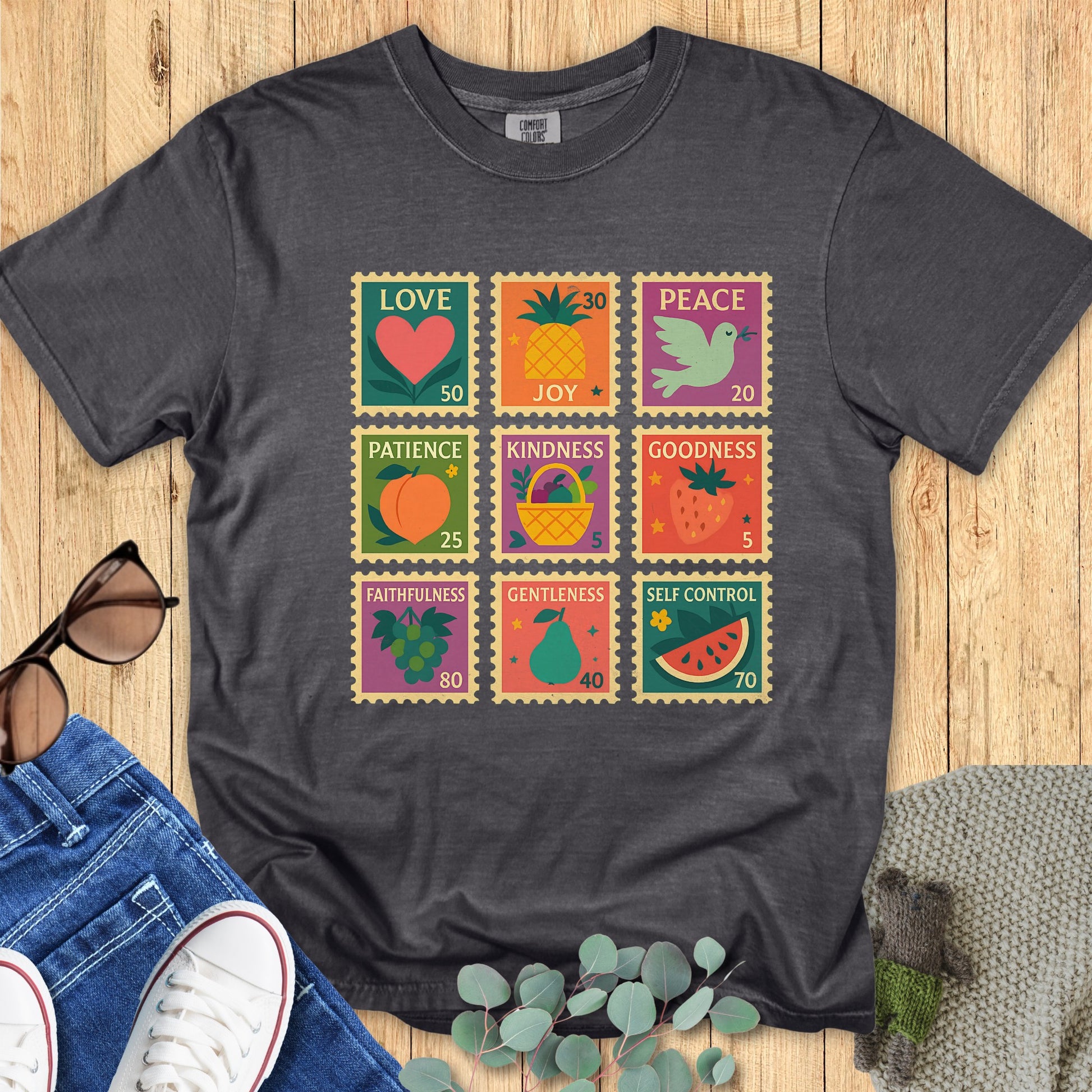 Flat lay of a Comfort Colors Christian T-shirt in pepper gray, decorated with retro-style Fruit of the Spirit stamp blocks highlighting love, joy, peace, patience, kindness, goodness, faithfulness, gentleness, and self-control.