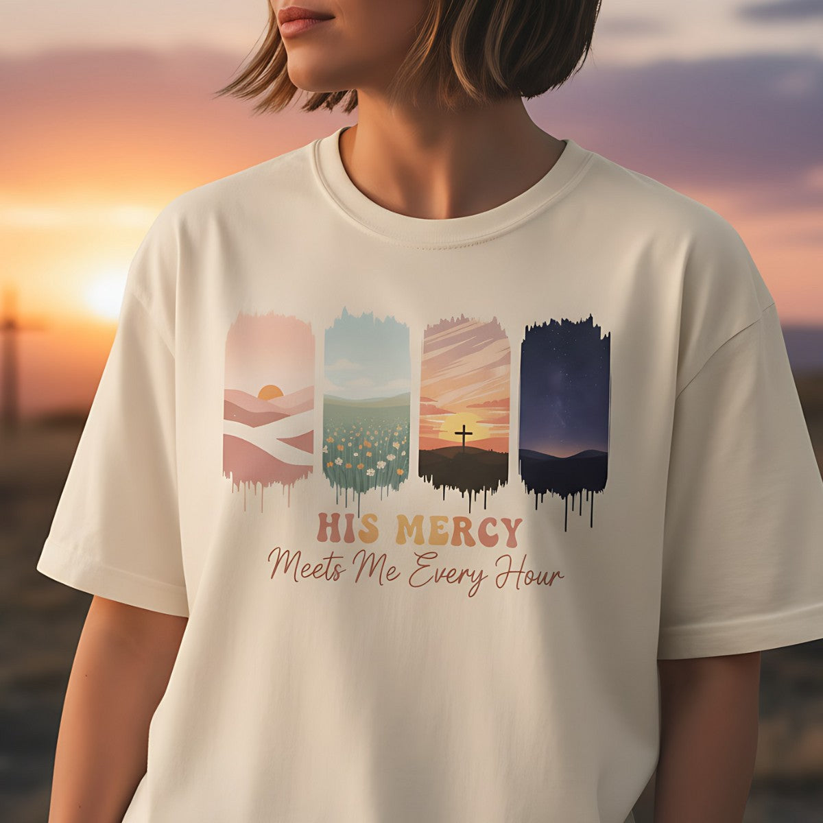 Comfort Colors Christian t-shirt in ivory with faith-inspired print “His Mercy Meets Me Every Hour.” Illustrated four-panel artwork includes sunrise desert, tulip field, sunset cross, and night sky. Lifestyle photo of woman wearing shirt outdoors at sunset with cross in background, highlighting Christian encouragement style.