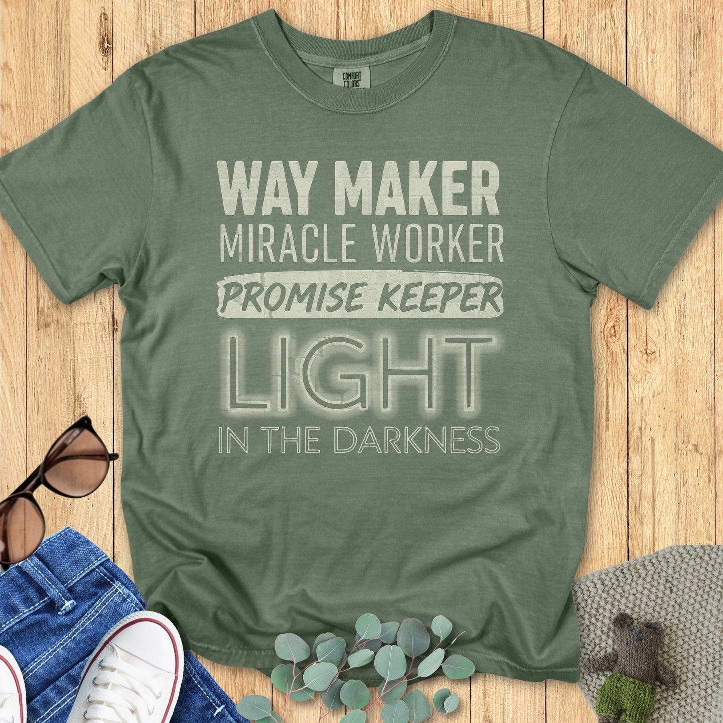 Comfort Colors Christian t-shirt in moss green with inspirational worship lyrics 'Way Maker, Miracle Worker, Promise Keeper, Light in the Darkness.' Relaxed Christian apparel mockup perfect for faith-based outfits.