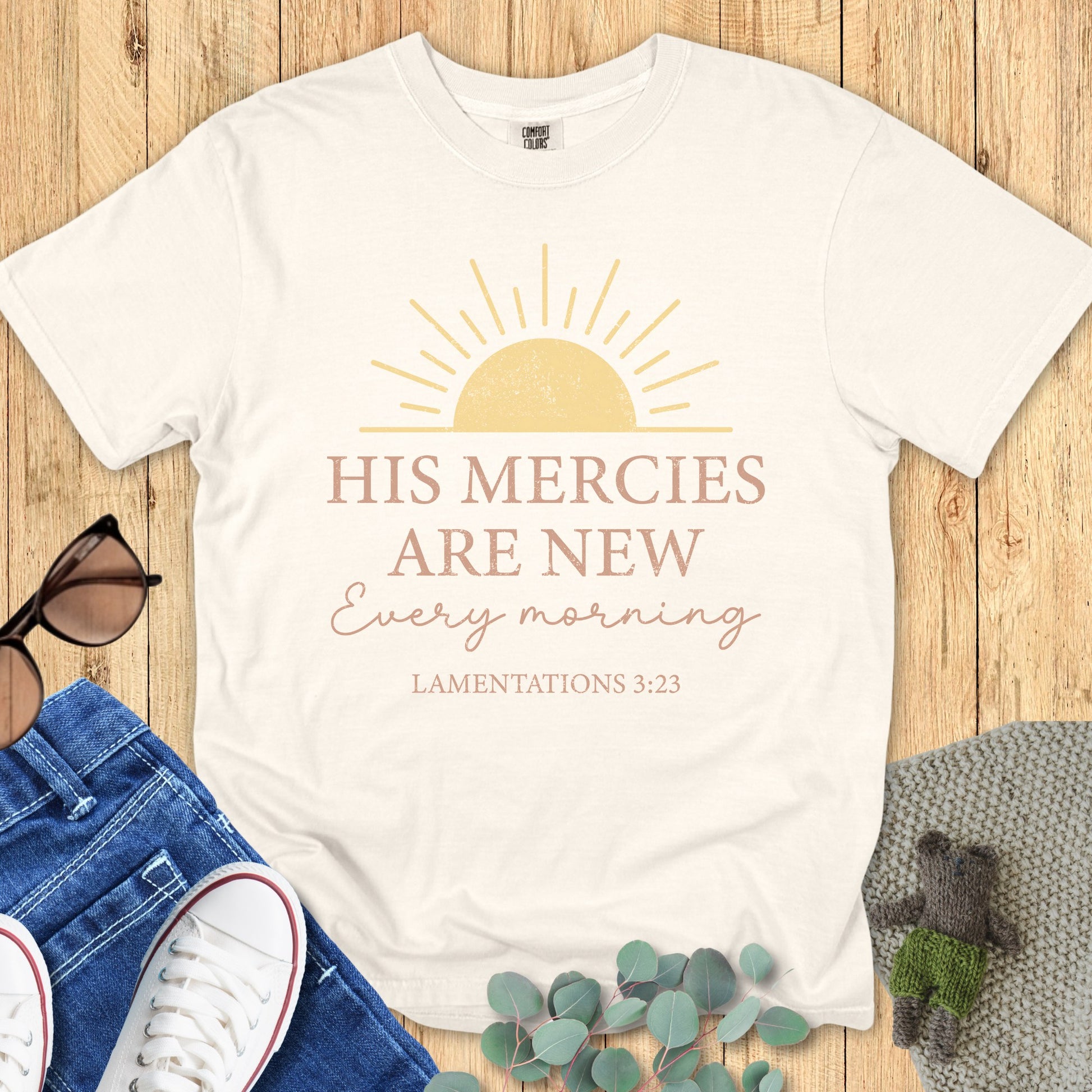 Flatlay of a Comfort Colors 1717 ivory “His Mercies Are New Every Morning – Lamentations 3:23” t-shirt paired with jeans and sneakers. A faith-based apparel for women piece with uplifting scripture design.