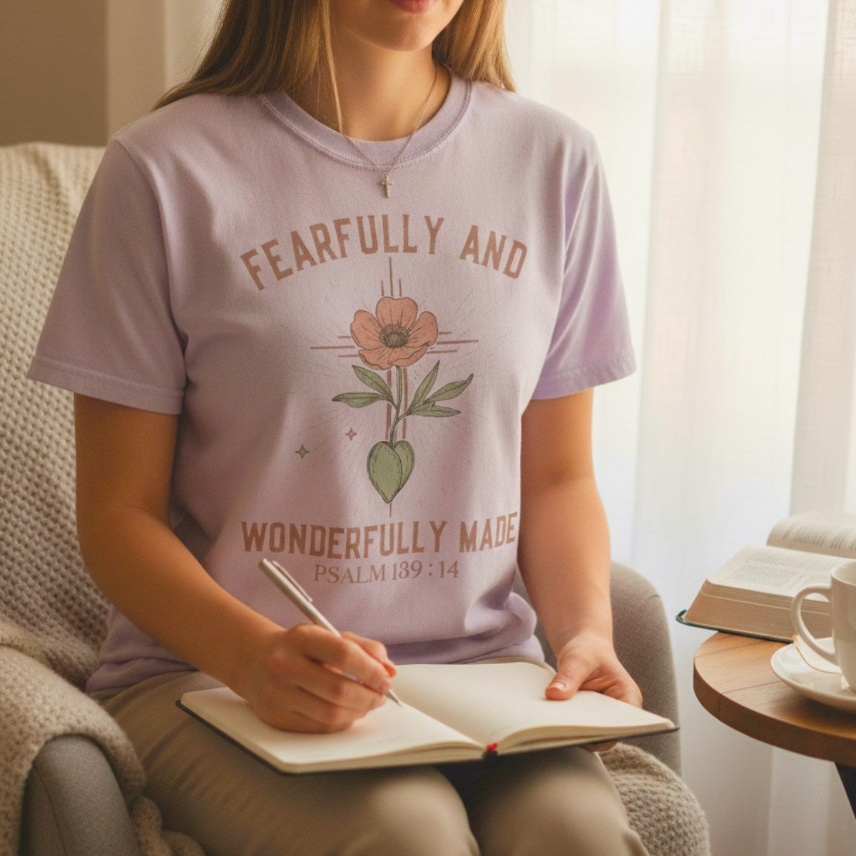 Woman journaling at home while wearing a Comfort Colors 1717 orchid “Fearfully and Wonderfully Made – Psalm 139:14” t-shirt. A peaceful, feminine piece from women’s scripture tees, perfect as a Christian mom gift idea.