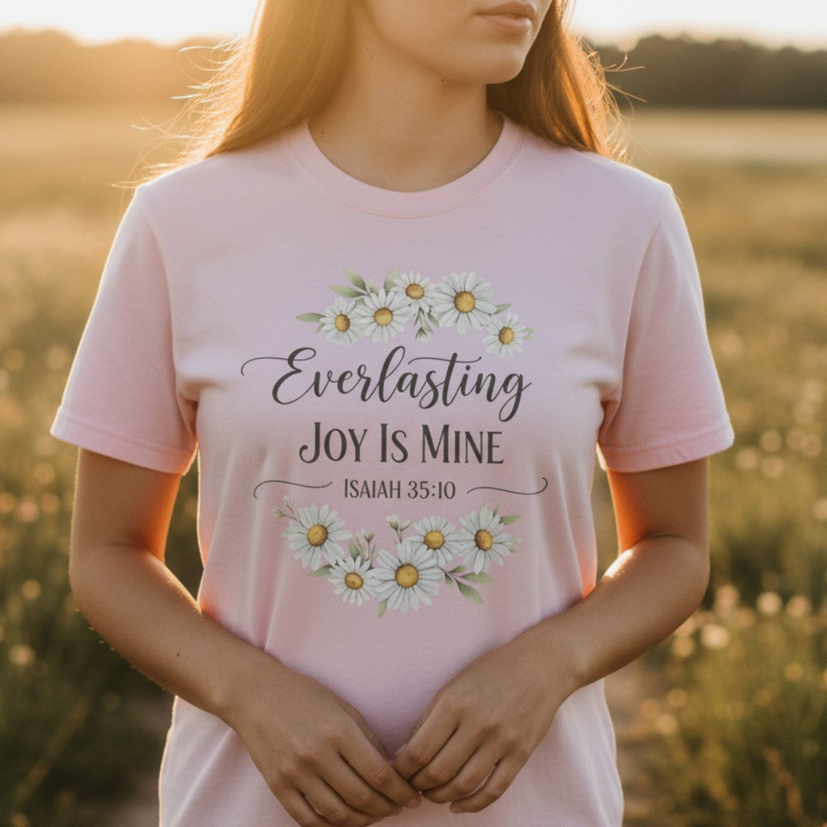 Woman standing in a sunlit field wearing a Comfort Colors 1717 blossom pink “Everlasting Joy Is Mine – Isaiah 35:10” t-shirt. A joyful women’s scripture tee perfect for daily inspiration or thoughtful Christian mom gift ideas.