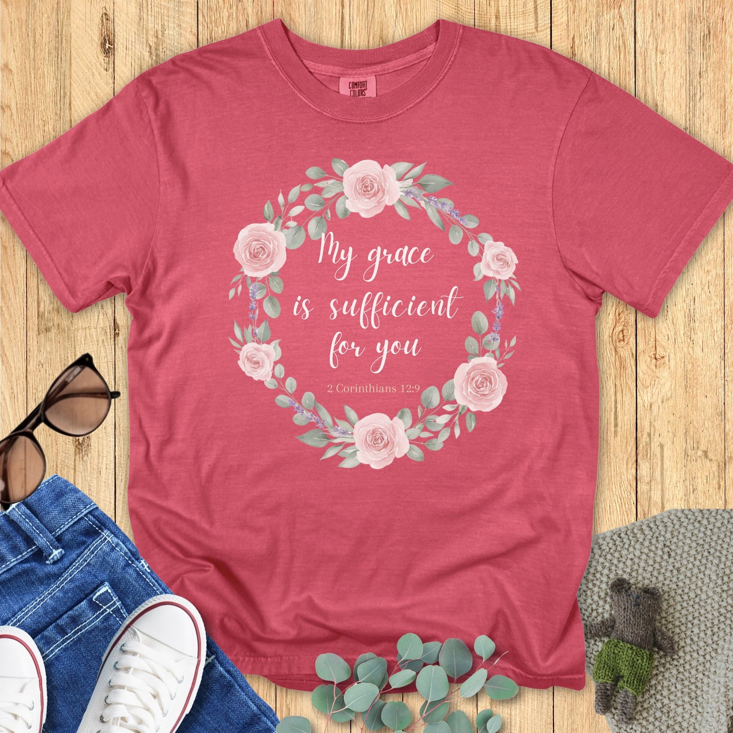 Flatlay of a Comfort Colors 1717 crimson “My Grace Is Sufficient for You – 2 Corinthians 12:9” t-shirt styled with casual accessories. A modern Christian shirt for women celebrating divine grace and strength.