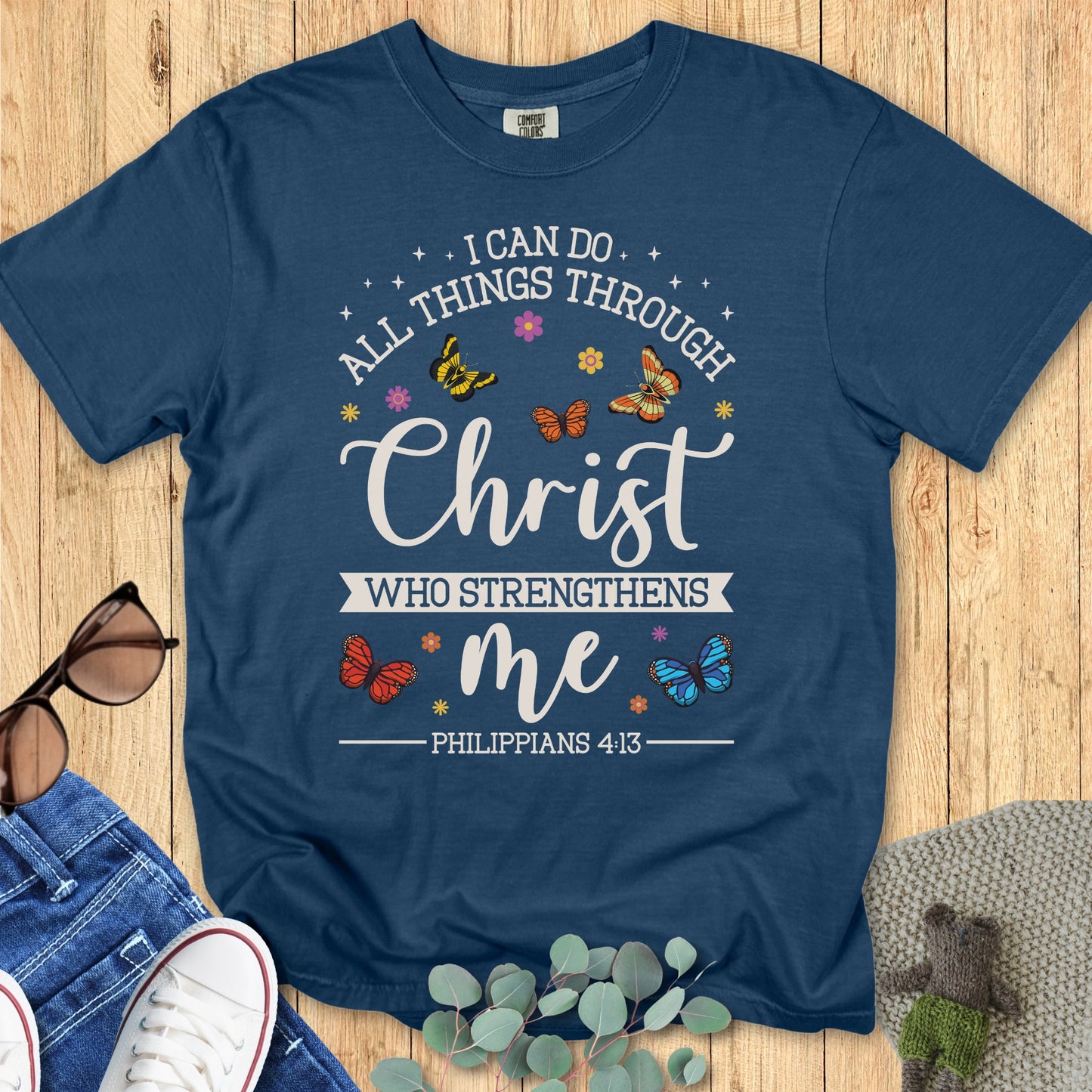 Flatlay of a Comfort Colors 1717 midnight “I Can Do All Things Through Christ Who Strengthens Me – Philippians 4:13” t-shirt. This elegant women’s scripture tee combines colorful butterfly motifs with encouraging scripture for stylish faith-based apparel.