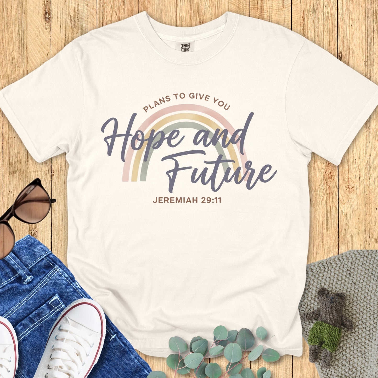 Flatlay of a Comfort Colors 1717 ivory “Hope and Future – Jeremiah 29:11” t-shirt featuring a soft pastel rainbow and elegant script text. A gentle, uplifting women’s scripture tee — modern faith-based apparel for women and a thoughtful Christian mom gift idea.