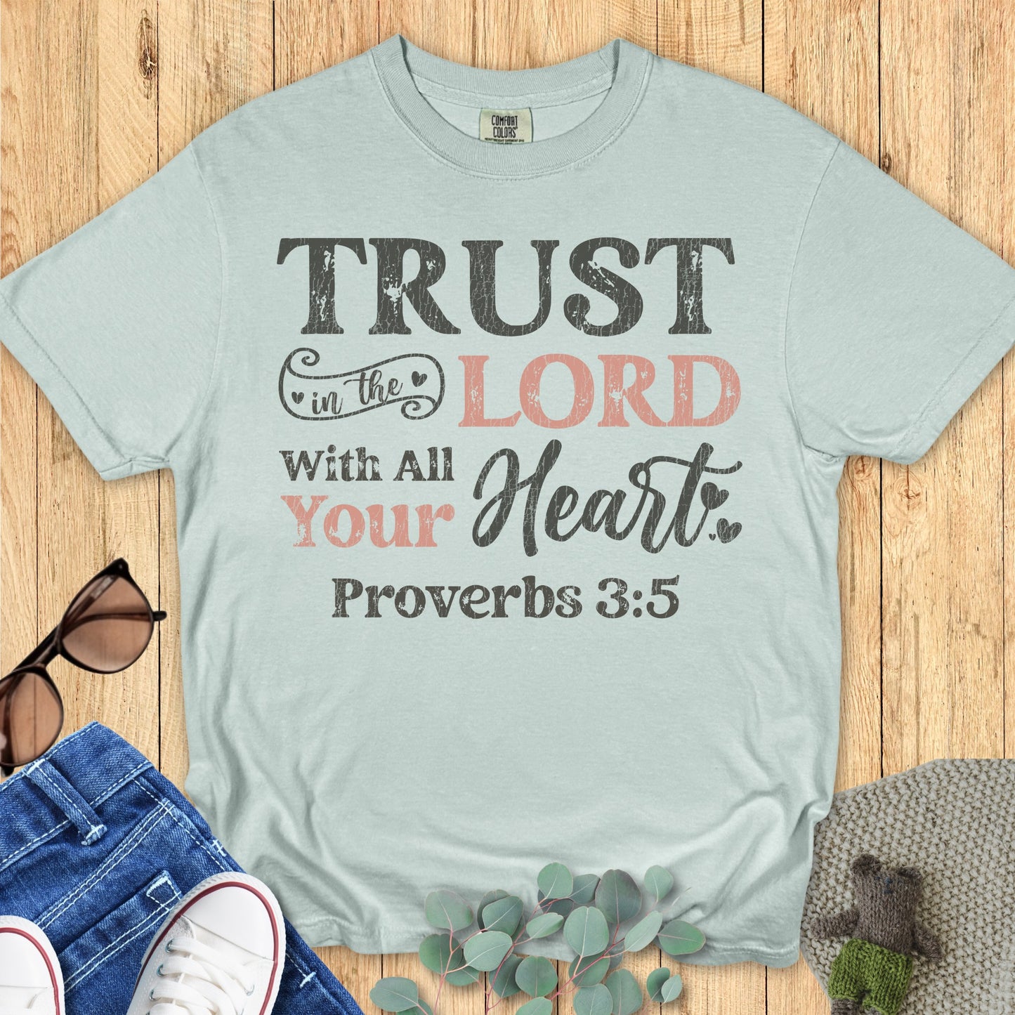 Flatlay of a Comfort Colors 1717 bay “Trust in the Lord with all your heart – Proverbs 3:5” t-shirt with rustic black and blush text. A beautiful women’s scripture tee — soft faith-based apparel for women and thoughtful Christian mom gift idea.