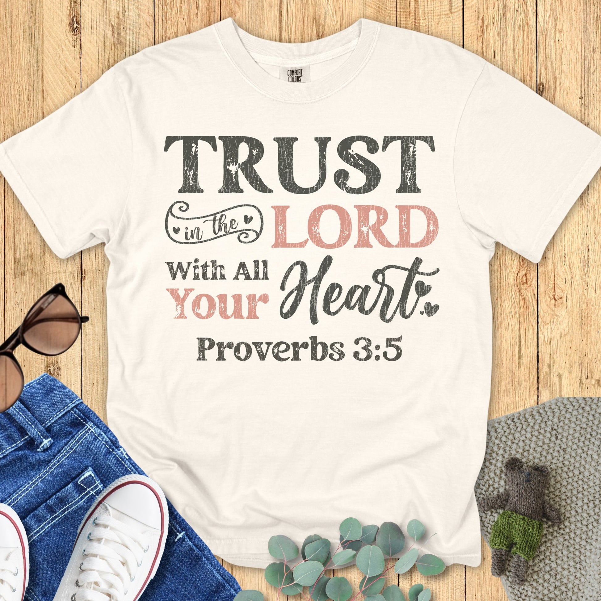 Flatlay of a Comfort Colors 1717 ivory “Trust in the Lord with all your heart – Proverbs 3:5” t-shirt with vintage typography. A clean and classic women’s scripture tee — uplifting faith-based apparel for women and elegant Christian mom gift idea.