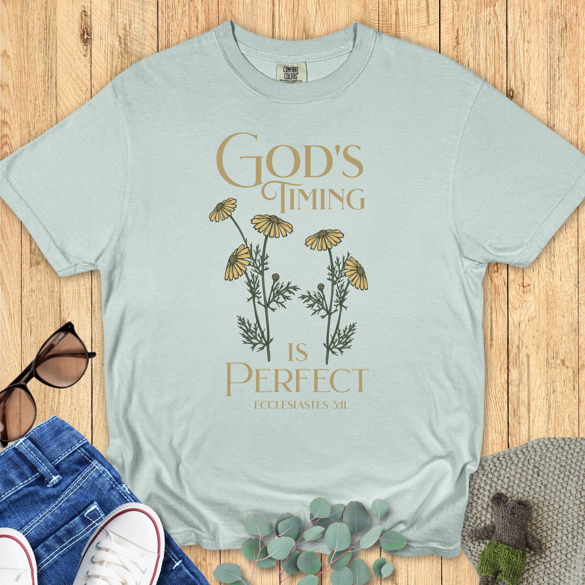 Flatlay of a Comfort Colors 1717 bay “God’s Timing Is Perfect – Ecclesiastes 3:11” t-shirt with elegant gold typography and daisy flower art. A peaceful and stylish women’s scripture tee — modern faith-based apparel for women and meaningful Christian mom gift idea.
