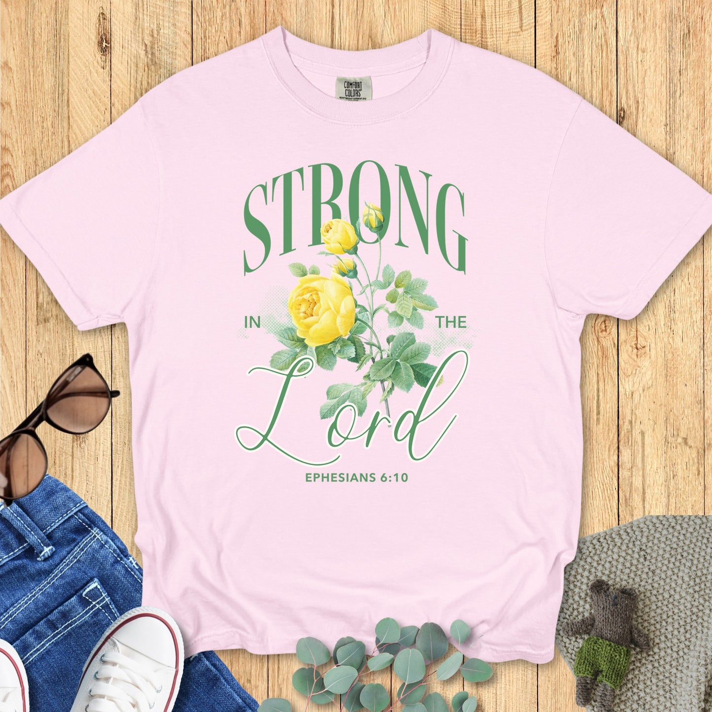 Flatlay of a Comfort Colors 1717 blossom “Strong in the Lord – Ephesians 6:10” t-shirt featuring vintage-style yellow floral design. A feminine and faith-filled women’s scripture tee — uplifting faith-based apparel for women and perfect Christian mom gift.