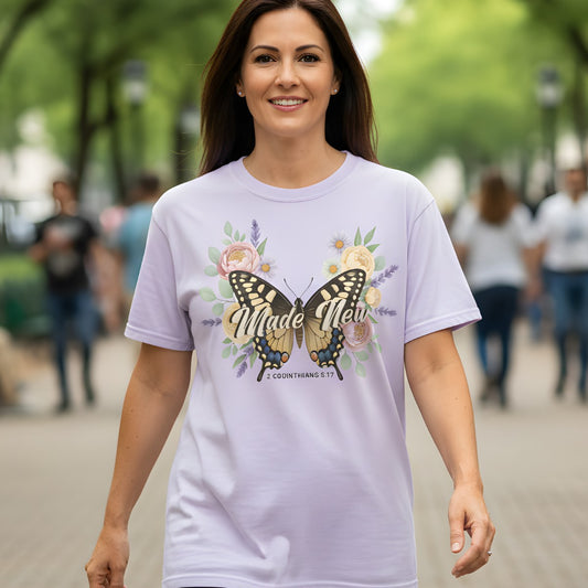 Woman walking outdoors wearing a Comfort Colors 1717 orchid βMade New β 2 Corinthians 5:17β t-shirt with butterfly and floral artwork. A refreshing and hope-filled womenβs scripture tee β stylish modern Christian shirt and faith-based apparel for women.