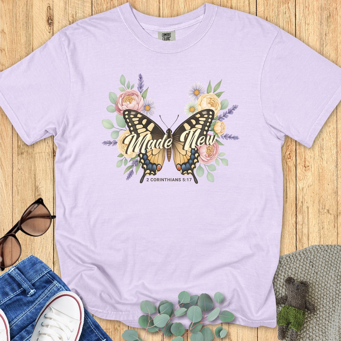 latlay of a Comfort Colors 1717 orchid “Made New – 2 Corinthians 5:17” t-shirt featuring a butterfly surrounded by soft floral blooms. A beautiful and uplifting women’s scripture tee — modern Christian shirt and faith-based apparel for women, perfect Christian mom gift idea.