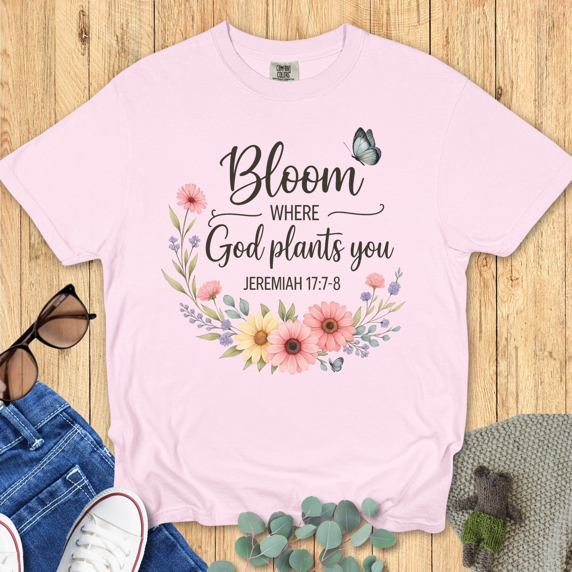Flatlay of a Comfort Colors 1717 ivory “Bloom Where God Plants You – Jeremiah 17:7-8” t-shirt featuring pastel wildflowers and butterflies. A soft and feminine women’s scripture tee — modern Christian shirt and uplifting faith-based apparel for women, perfect Christian mom gift idea.