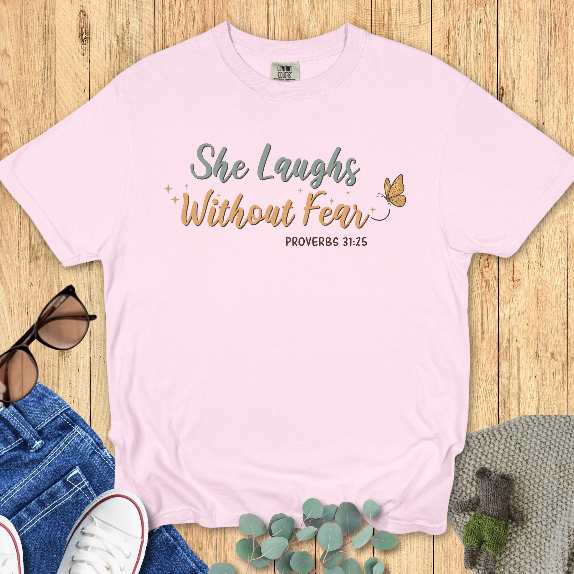 Comfort Colors 1717 blossom “She Laughs Without Fear – Proverbs 31:25” t-shirt in pastel pink with elegant lettering and delicate butterfly detail. A feminine women’s scripture tee — uplifting modern Christian shirt and perfect faith-based apparel for women.