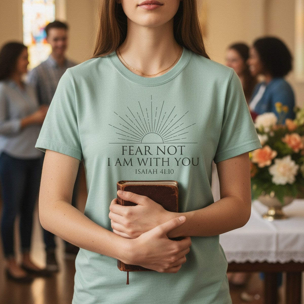 Woman holding a Bible while wearing a Comfort Colors 1717 bay green “Fear Not I Am With You – Isaiah 41:10” t-shirt inside a church. A peaceful women’s scripture tee — elegant faith-based apparel for women and uplifting modern Christian shirt, perfect Christian mom gift idea.