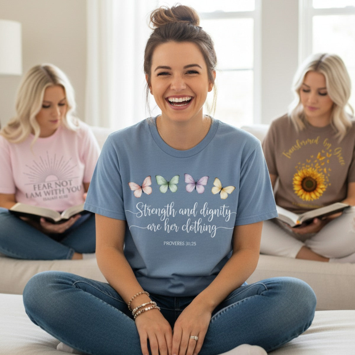 Smiling woman wearing a Comfort Colors 1717 blue jean “Strength and dignity are her clothing – Proverbs 31:25” t-shirt surrounded by friends studying the Bible. A joyful women’s scripture tee — uplifting faith-based apparel for women and modern Christian shirt, perfect Christian mom gift idea.