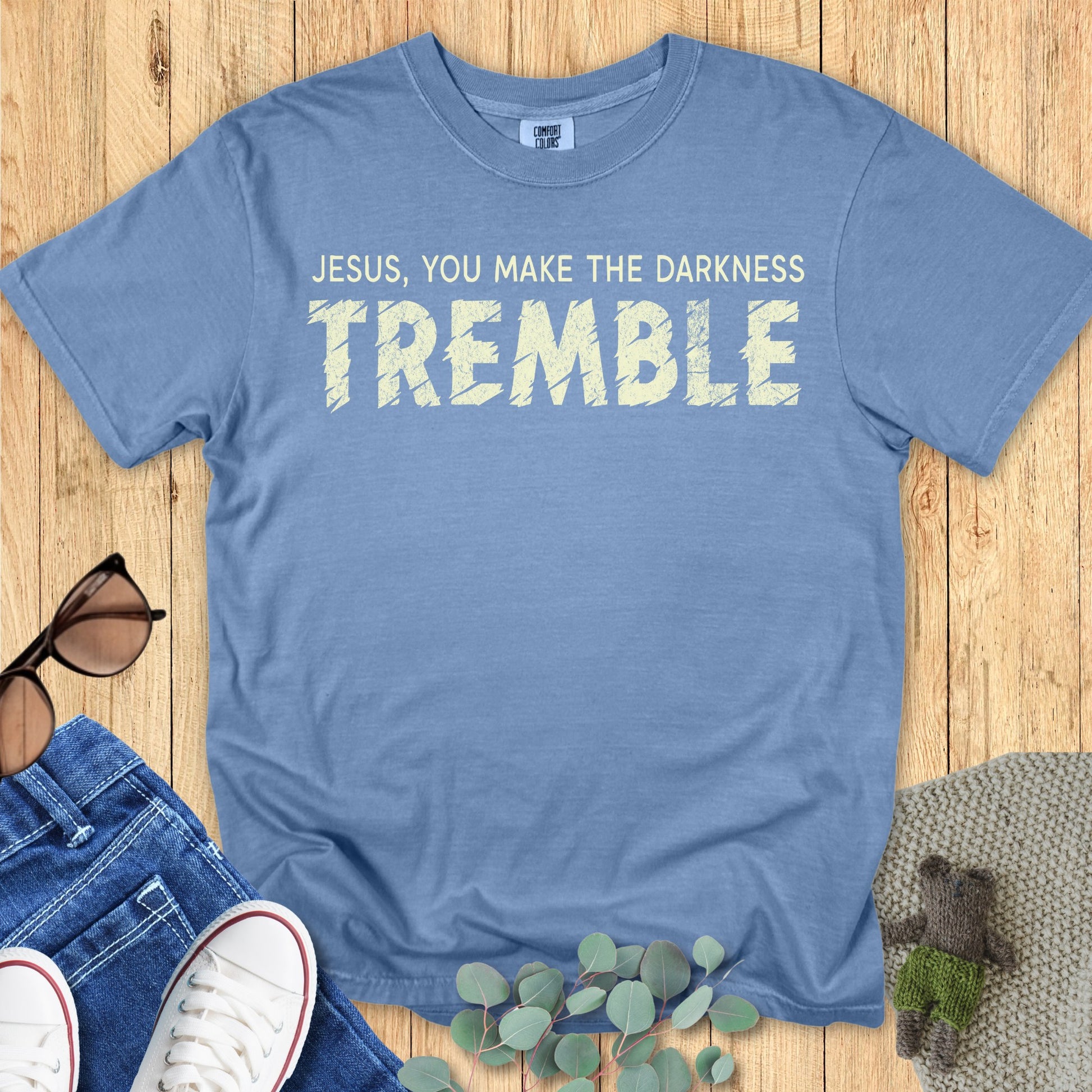 Flatlay of a Comfort Colors 1717 blue jean “Jesus, You Make the Darkness Tremble” t-shirt featuring bold distressed typography. A stylish women’s scripture tee — meaningful faith-based apparel for women and modern Christian shirt, ideal Christian mom gift idea.