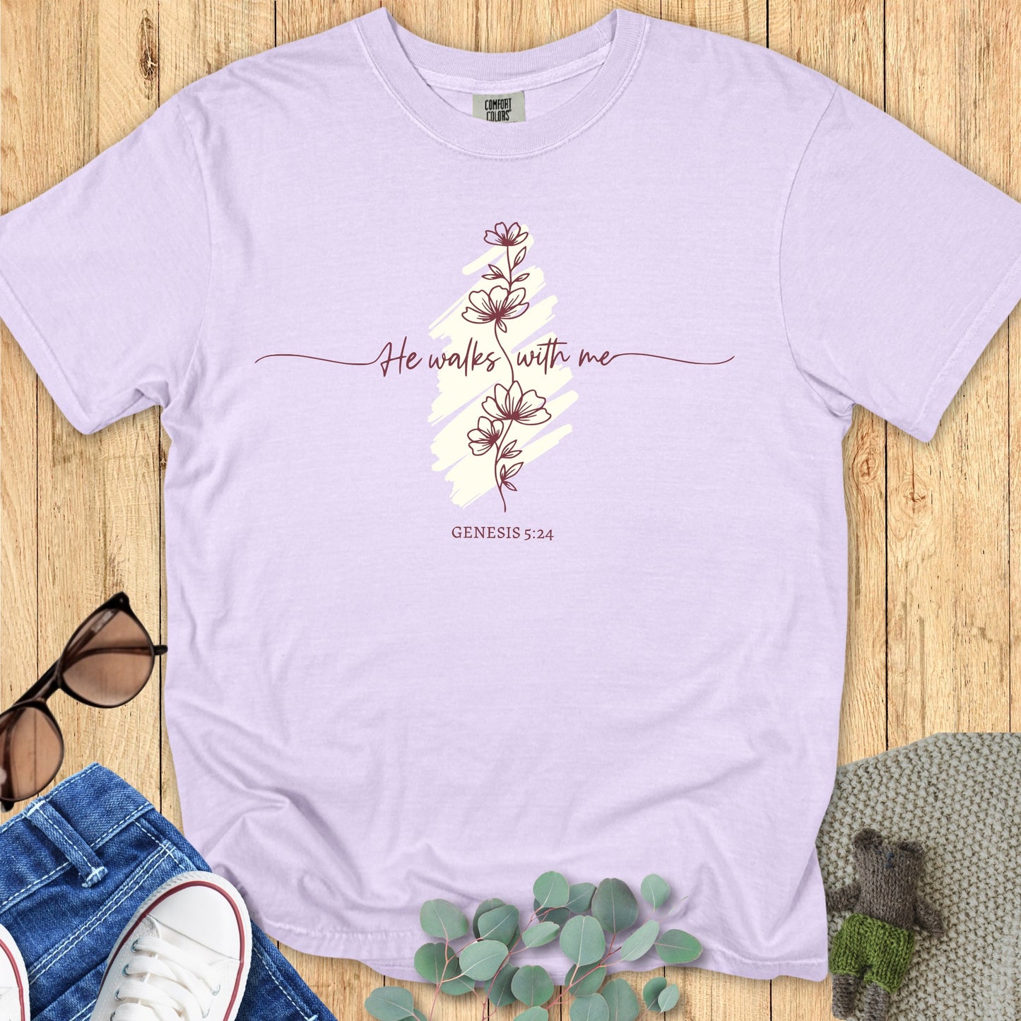 Flatlay of a Comfort Colors 1717 orchid “He Walks With Me – Genesis 5:24” t-shirt with hand-drawn floral line art and soft brush background. A gentle women’s scripture tee — elegant faith-based apparel for women and modern Christian shirt, thoughtful Christian mom gift idea.