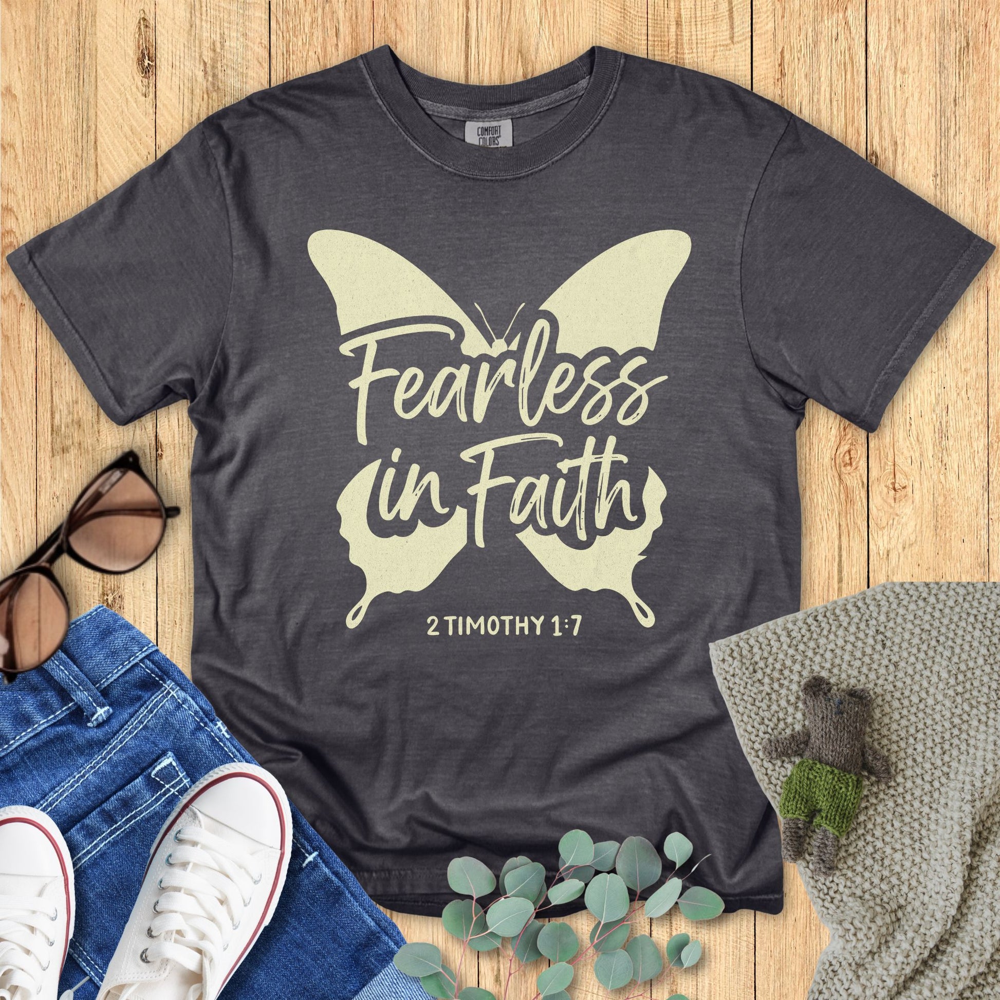 Flatlay of a Comfort Colors 1717 pepper “Fearless in Faith – 2 Timothy 1:7” t-shirt featuring a large butterfly graphic and hand-lettered script. A powerful women’s scripture tee — stylish faith-based apparel for women and modern Christian shirt, great Christian mom gift idea.