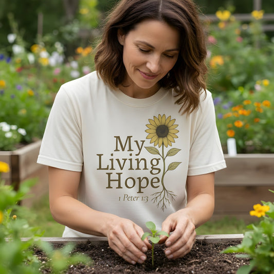 Woman gardening while wearing a Comfort Colors 1717 ivory βMy Living Hope β 1 Peter 1:3β t-shirt featuring a sunflower with roots design. A soft and uplifting womenβs scripture tee β faith-based apparel for women and modern Christian shirt, thoughtful Christian mom gift idea.