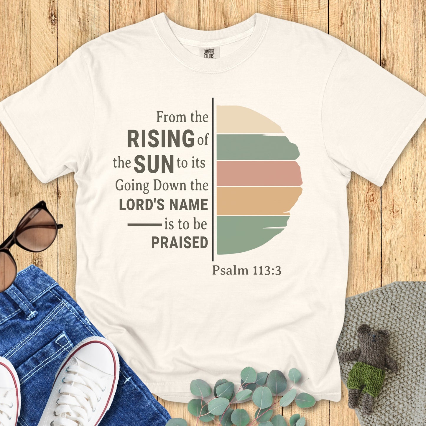 Flatlay of a Comfort Colors 1717 ivory “From the Rising of the Sun to its Going Down, the Lord’s Name is to be Praised – Psalm 113:3” t-shirt featuring a minimalist sun design in warm earthy tones. A stylish women’s scripture tee — faith-based apparel for women and modern Christian shirt, thoughtful Christian mom gift idea.