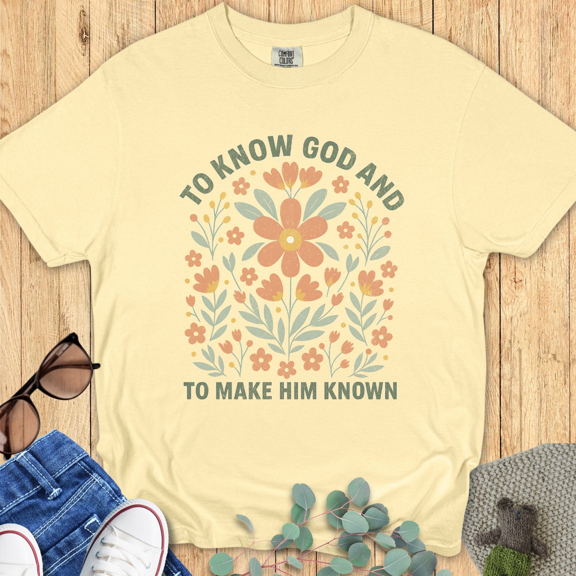 Flatlay of a Comfort Colors 1717 butter “To Know God and To Make Him Known” t-shirt featuring cheerful vintage-style flowers. A bright and meaningful women’s scripture tee — faith-based apparel for women and modern Christian shirt, great Christian mom gift idea.