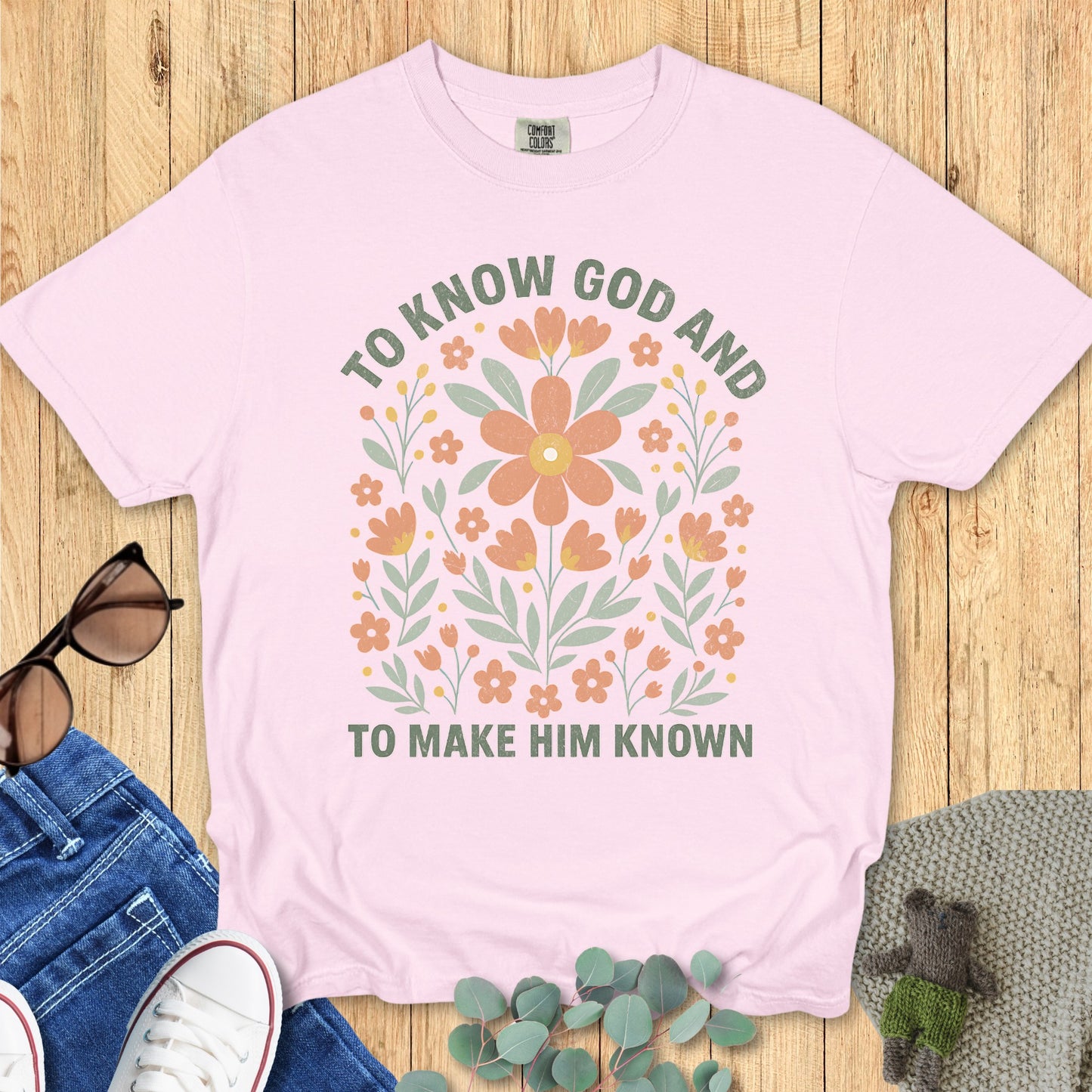 Flatlay of a Comfort Colors 1717 blossom “To Know God and To Make Him Known” t-shirt with hand-drawn floral illustration. A feminine women’s scripture tee — inspiring faith-based apparel for women and modern Christian shirt, perfect Christian mom gift idea.