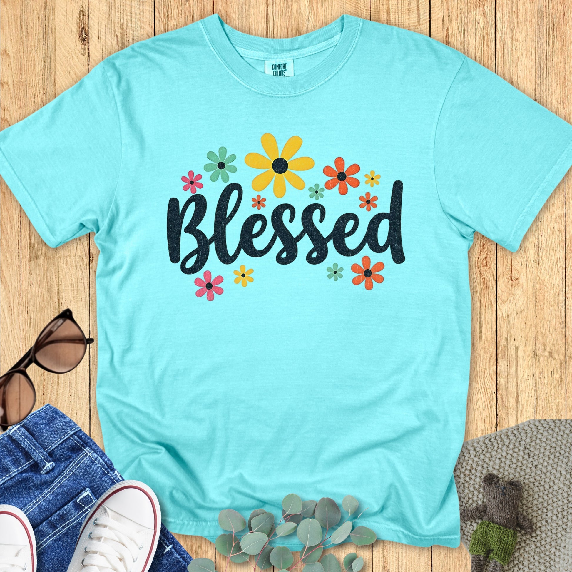 Flatlay of a Comfort Colors 1717 chalky mint “Blessed” t-shirt featuring bold script text surrounded by colorful flowers. A cheerful women’s scripture tee — faith-based apparel for women and modern Christian shirt, perfect Christian mom gift idea for spring or summer.