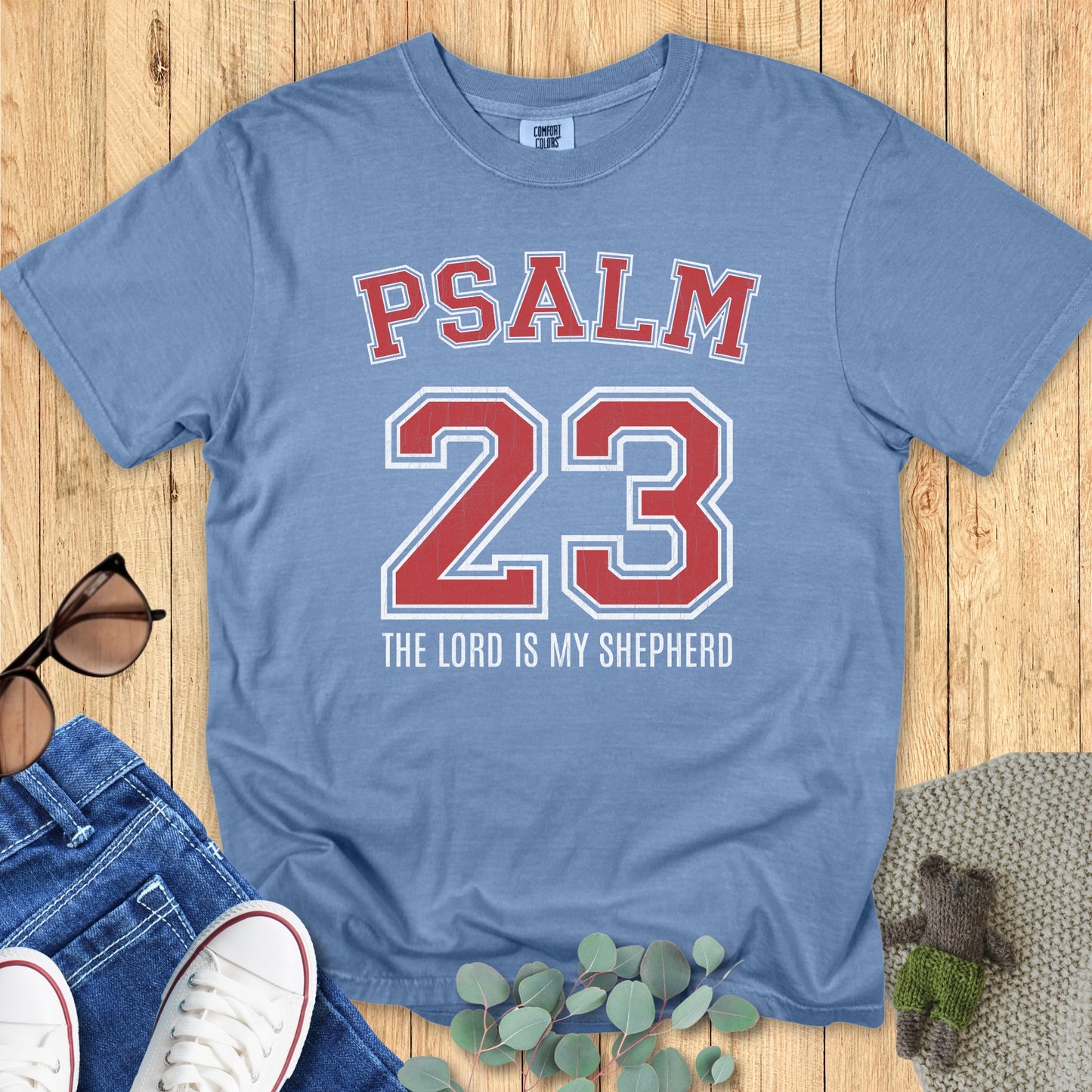 latlay of a Comfort Colors 1717 blue jean “Psalm 23 The Lord is My Shepherd” t-shirt with red varsity text and vintage lettering. A soft women’s scripture tee — faith-based apparel for women and modern Christian shirt, ideal Christian mom gift idea.