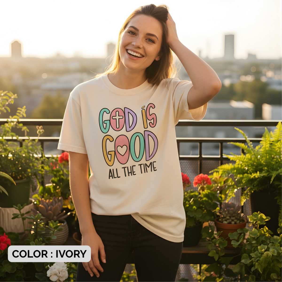Woman smiling in sunlight while wearing a Comfort Colors 1717 ivory “God Is Good All The Time” t-shirt with pastel block letters. A happy women’s scripture tee - faith-based apparel for women and modern Christian shirt, encouraging Christian mom gift idea for joyful believers.