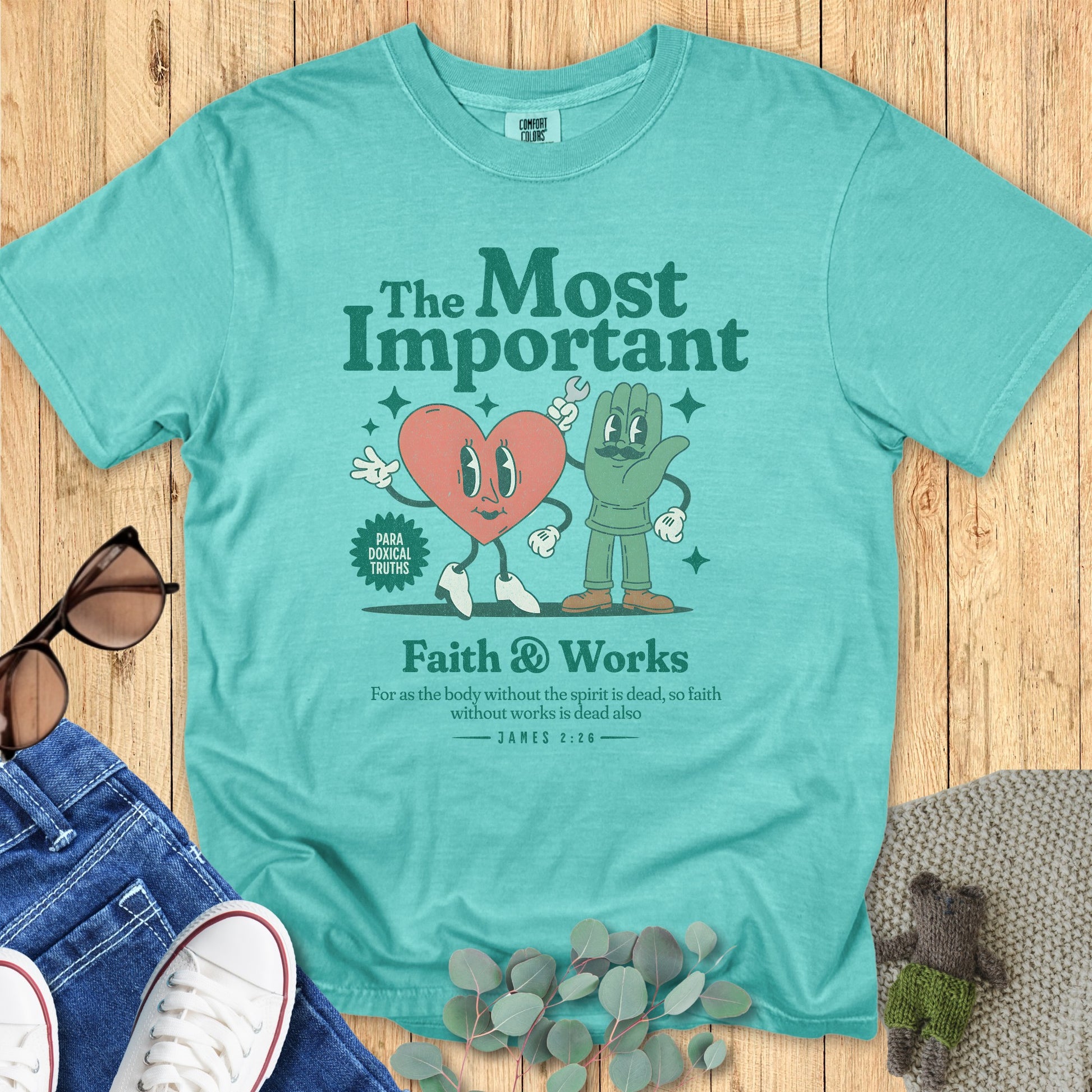 Flatlay of a Comfort Colors 1717 seafoam “Faith & Works” t-shirt featuring heart and hand cartoon characters with James 2:26 verse — “For as the body without the spirit is dead, so faith without works is dead also.” A cheerful women’s scripture tee -  faith-based apparel for women and modern Christian shirt, unique Christian mom gift idea.