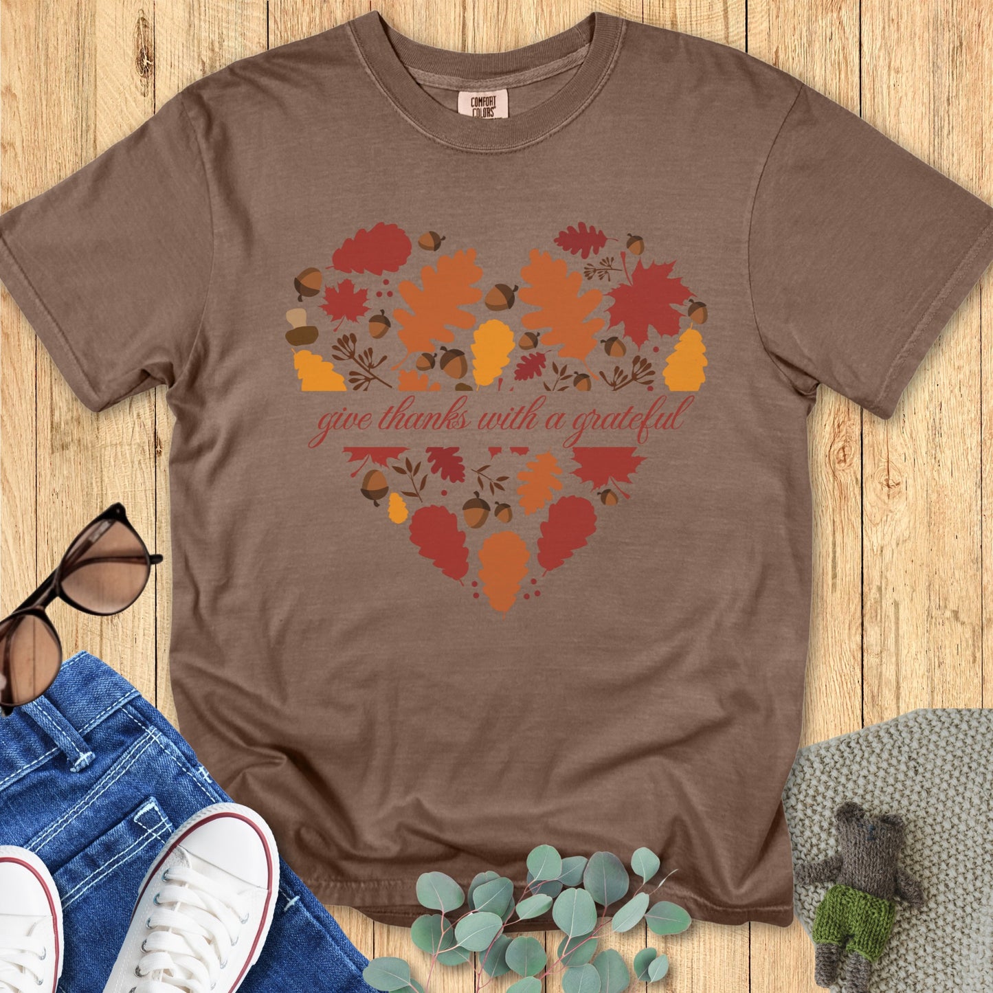 latlay of a Comfort Colors 1717 espresso “Give Thanks with a Grateful Heart” t-shirt with heart-shaped autumn leaf design. A cozy women’s scripture tee - faith-based apparel for women and modern Christian shirt, perfect Christian mom gift idea for showing gratitude this fall.