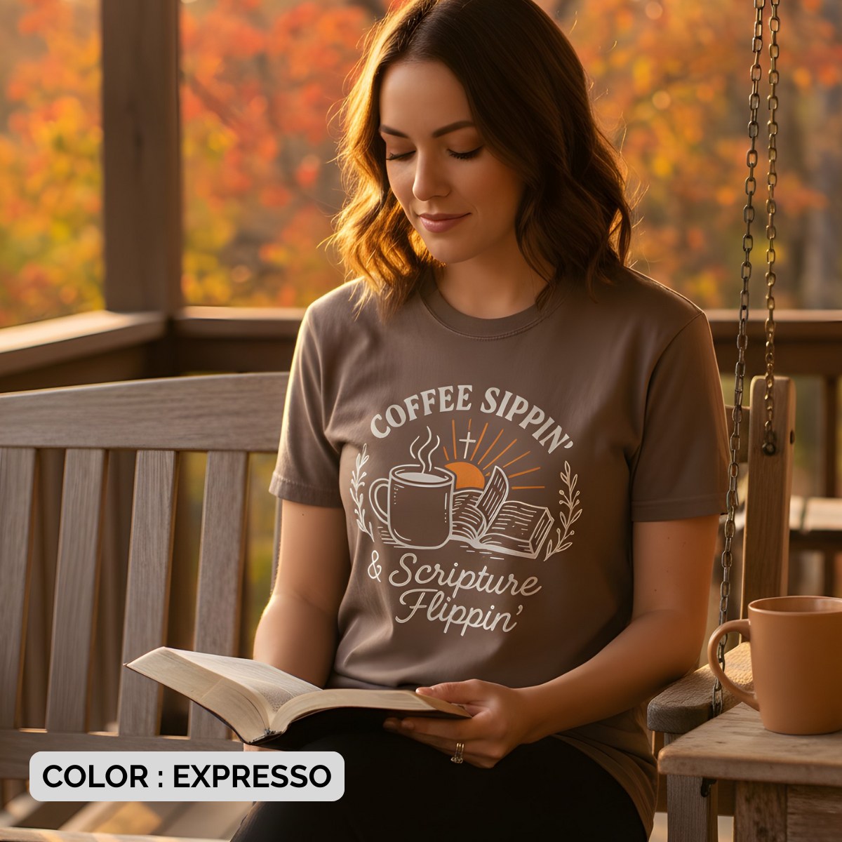 Woman sitting on a porch swing reading her Bible while wearing a Comfort Colors 1717 brown “Coffee Sippin’ & Scripture Flippin’” t-shirt. A cozy women’s scripture tee -  faith-based apparel for women and modern Christian shirt, perfect Christian mom gift idea for quiet morning devotion time.