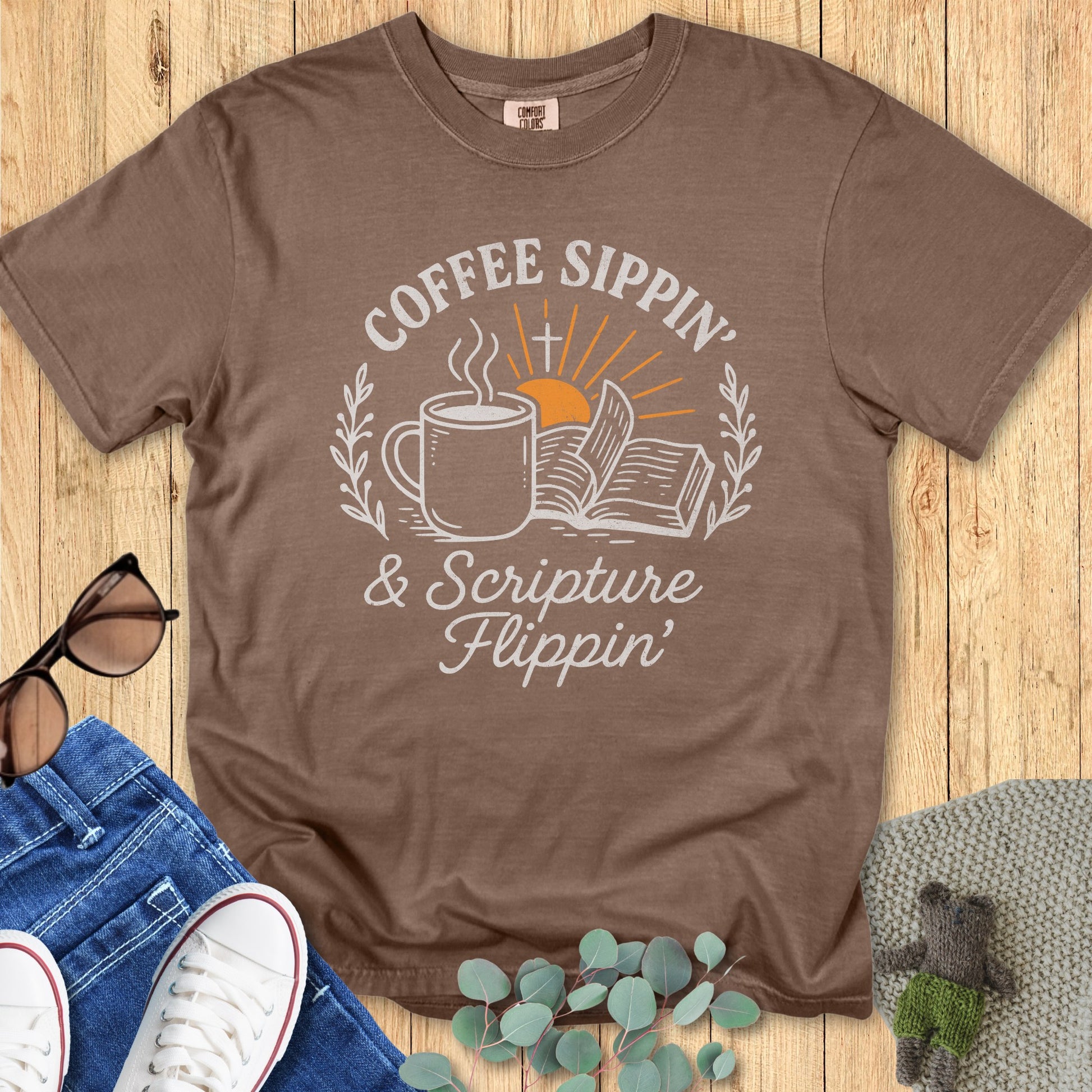 Flatlay of a Comfort Colors 1717 espresso “Coffee Sippin’ & Scripture Flippin’” t-shirt with cozy fall tones and hand-drawn coffee and Bible art. A casual women’s scripture tee - faith-based apparel for women and modern Christian shirt, charming Christian mom gift idea for daily devotions.