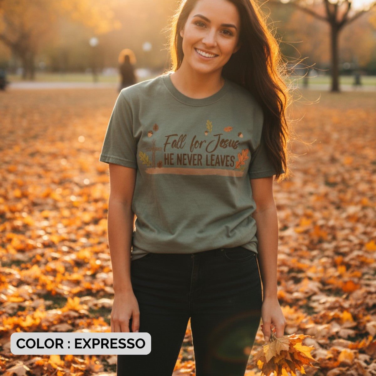Woman wearing a Comfort Colors 1717 espresso “Fall for Jesus, He Never Leaves” t-shirt surrounded by golden autumn leaves. A seasonal women’s scripture tee -  faith-based apparel for women and modern Christian shirt, thoughtful Christian mom gift idea celebrating faith and fall.