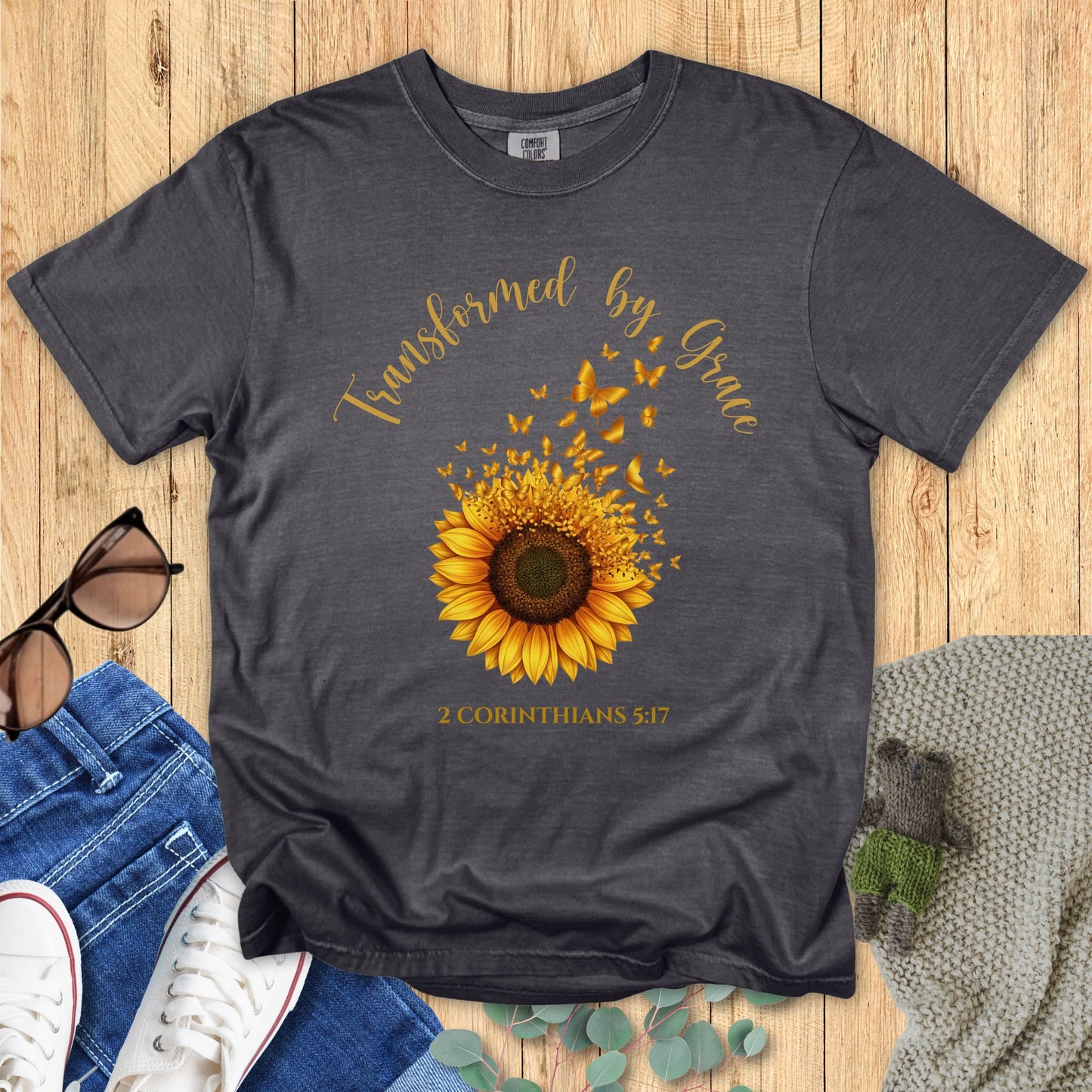 dark gray t-shirt with sunflower design and text on a wooden surface with jeans and sunglasses.