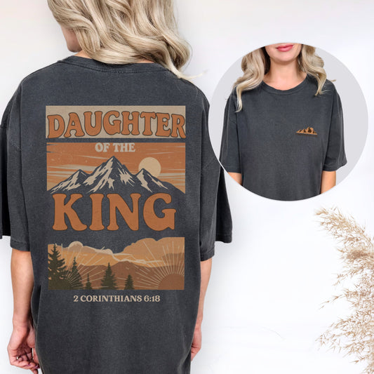 Person wearing a t-shirt with 'Daughter of the King' design and mountains on the back.