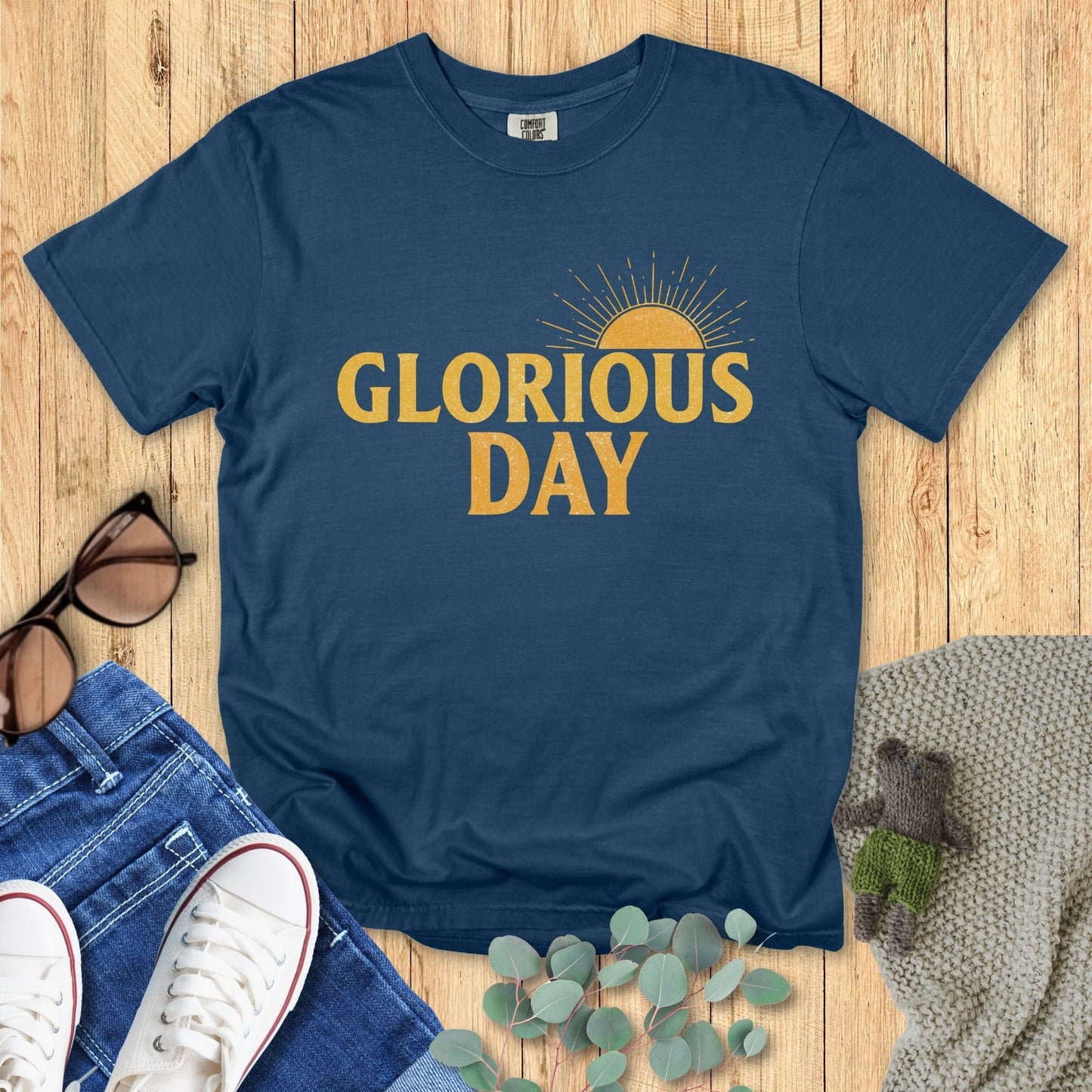Flatlay of a Comfort Colors 1717 midnight “Glorious Day” t-shirt showcasing a warm golden sunrise graphic. A timeless women’s scripture tee — soft and inspiring faith-based apparel for women and modern Christian shirt, meaningful Christian mom gift idea.