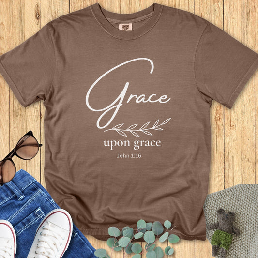 Flatlay of a Comfort Colors 1717 espresso “Grace Upon Grace – John 1:16” t-shirt designed with elegant white lettering and leaf motif. A cozy and inspiring women’s scripture tee ideal for daily wear or gifting.