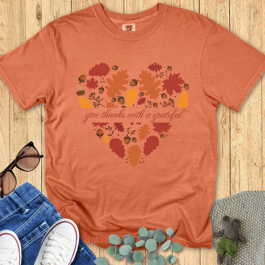 Flatlay of a Comfort Colors 1717 yam “Give Thanks with a Grateful Heart” t-shirt featuring a heart made of fall leaves and acorns. A warm women’s scripture tee - faith-based apparel for women and modern Christian shirt, thoughtful Christian mom gift idea for Thanksgiving or autumn days.