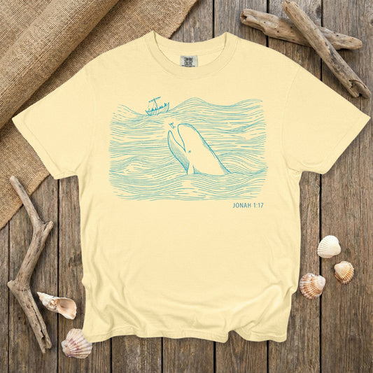 Comfort Colors 1717 butter yellow Christian women tee displaying a blue line-art illustration of Jonah and the great fish from Jonah 1:17. A bright and uplifting scripture-themed T-shirt designed for US faith wear and Christian women who enjoy playful Bible-story artwork.