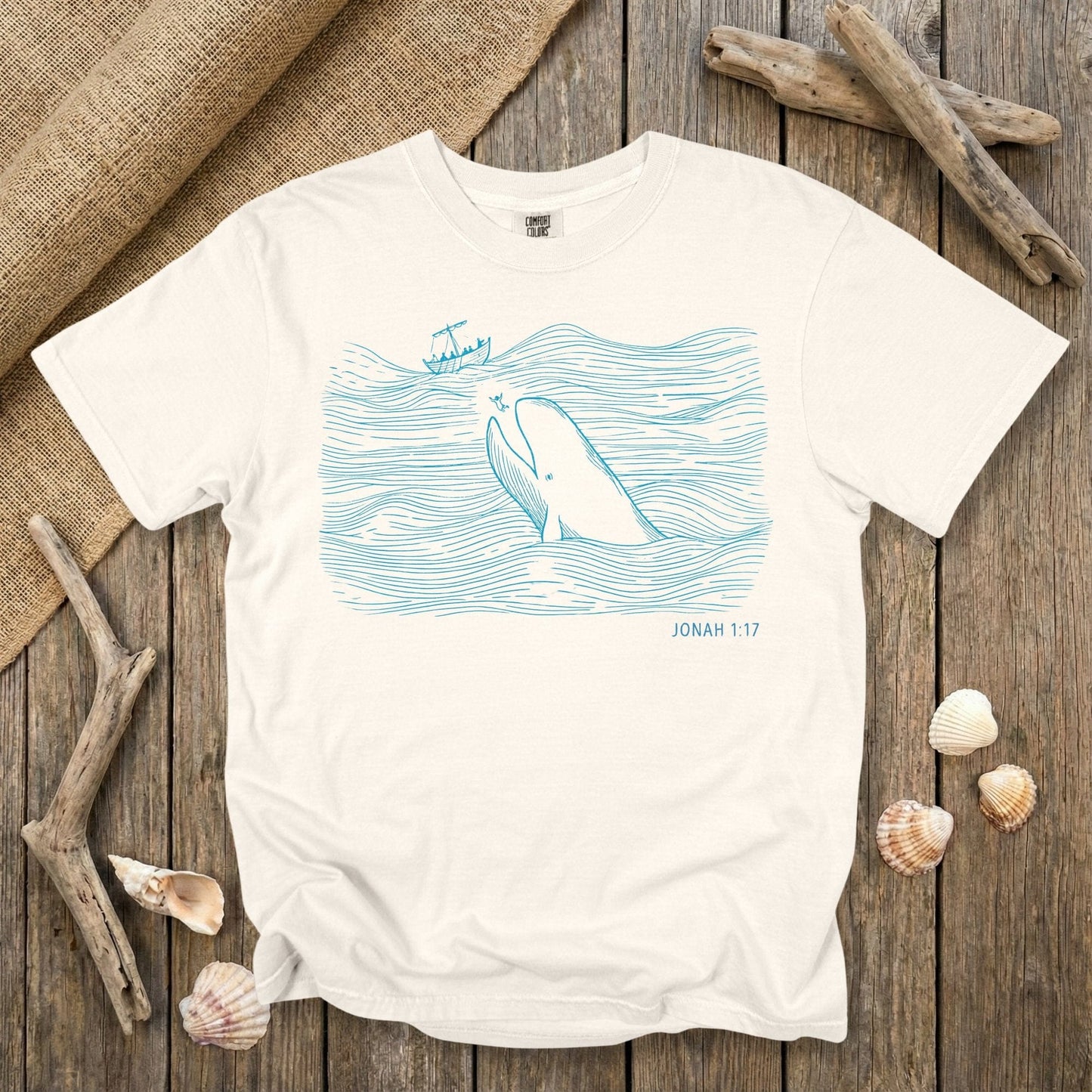 Comfort Colors 1717 ivory Christian women tee featuring a minimalist line-art illustration of Jonah and the great fish from Jonah 1:17, drawn in soft ocean-blue lines. A light, scripture-rooted US faith wear T-shirt perfect for women who love clean Biblical designs.
