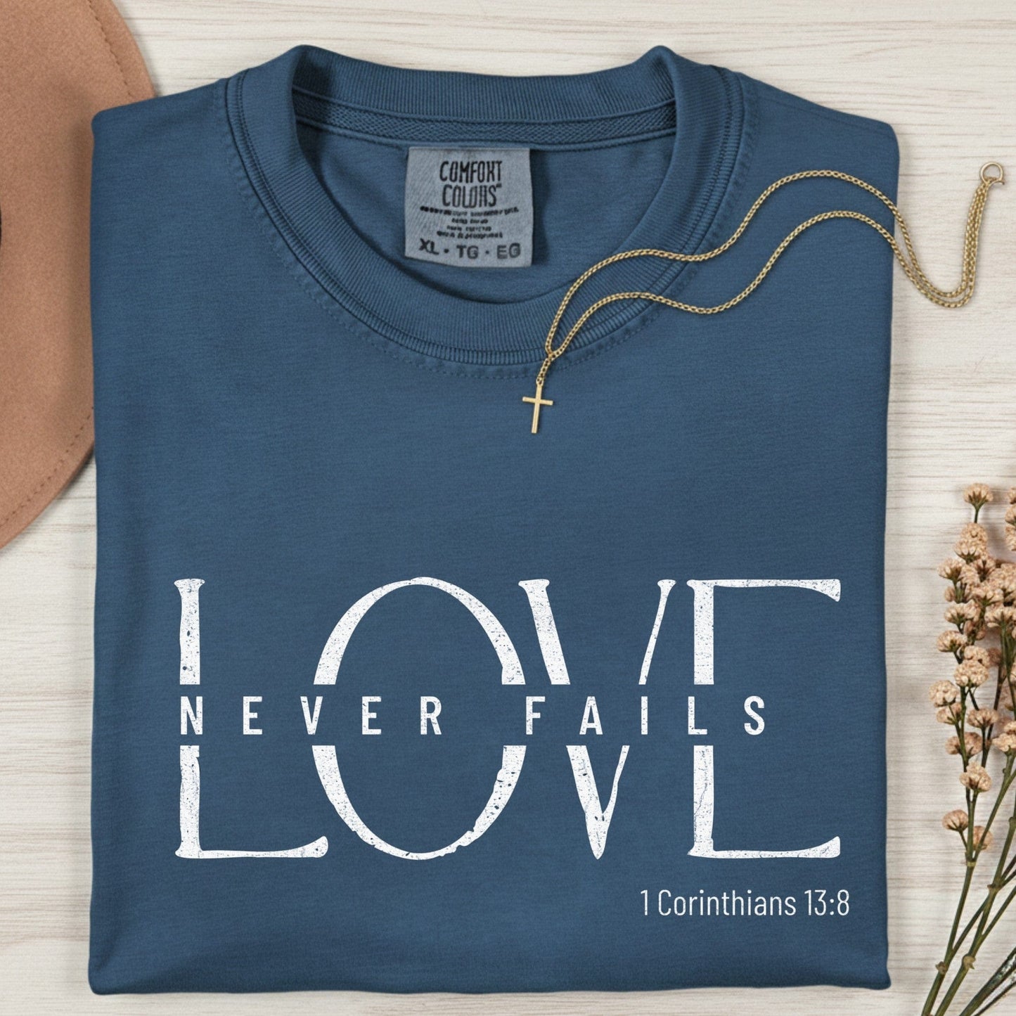Folded Comfort Colors 1717 midnight “Love Never Fails” t-shirt featuring clean white typography. A timeless women’s scripture tee — faith-based apparel for women and modern Christian shirt with 1 Corinthians 13:8 verse, perfect Christian mom gift idea.