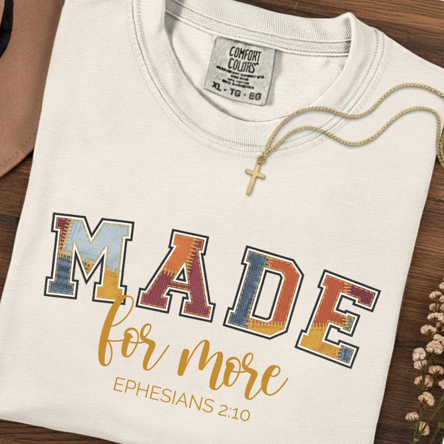 Flatlay of a Comfort Colors 1717 ivory “Made for More” Ephesians 2:10 t-shirt featuring colorful collegiate lettering and gold cursive text. A classic women’s scripture tee - faith-based apparel for women and modern Christian shirt, thoughtful Christian mom gift idea for encouragement and purpose.